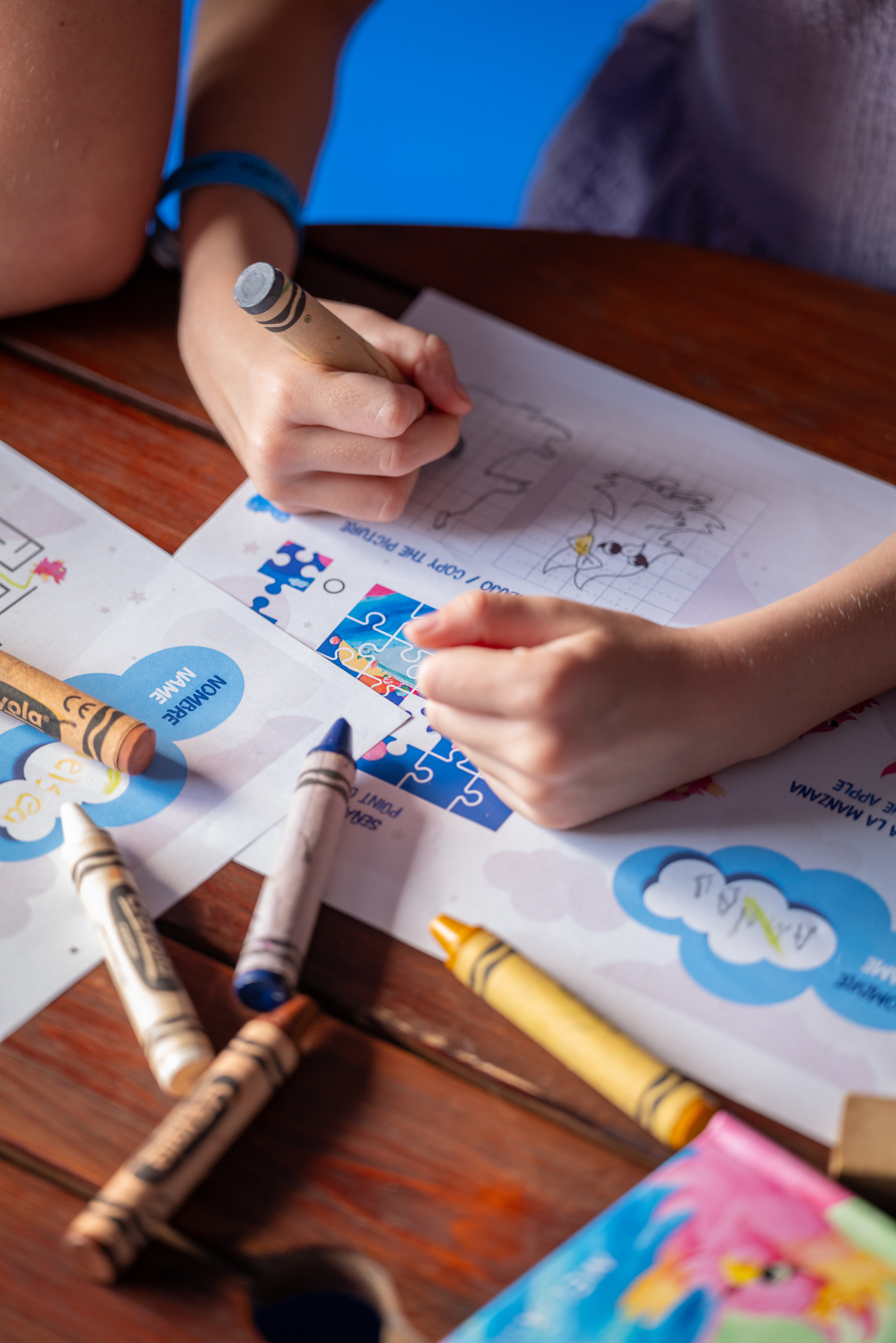 Manos de niño dibujando con crayones en hojas de actividades educativas.