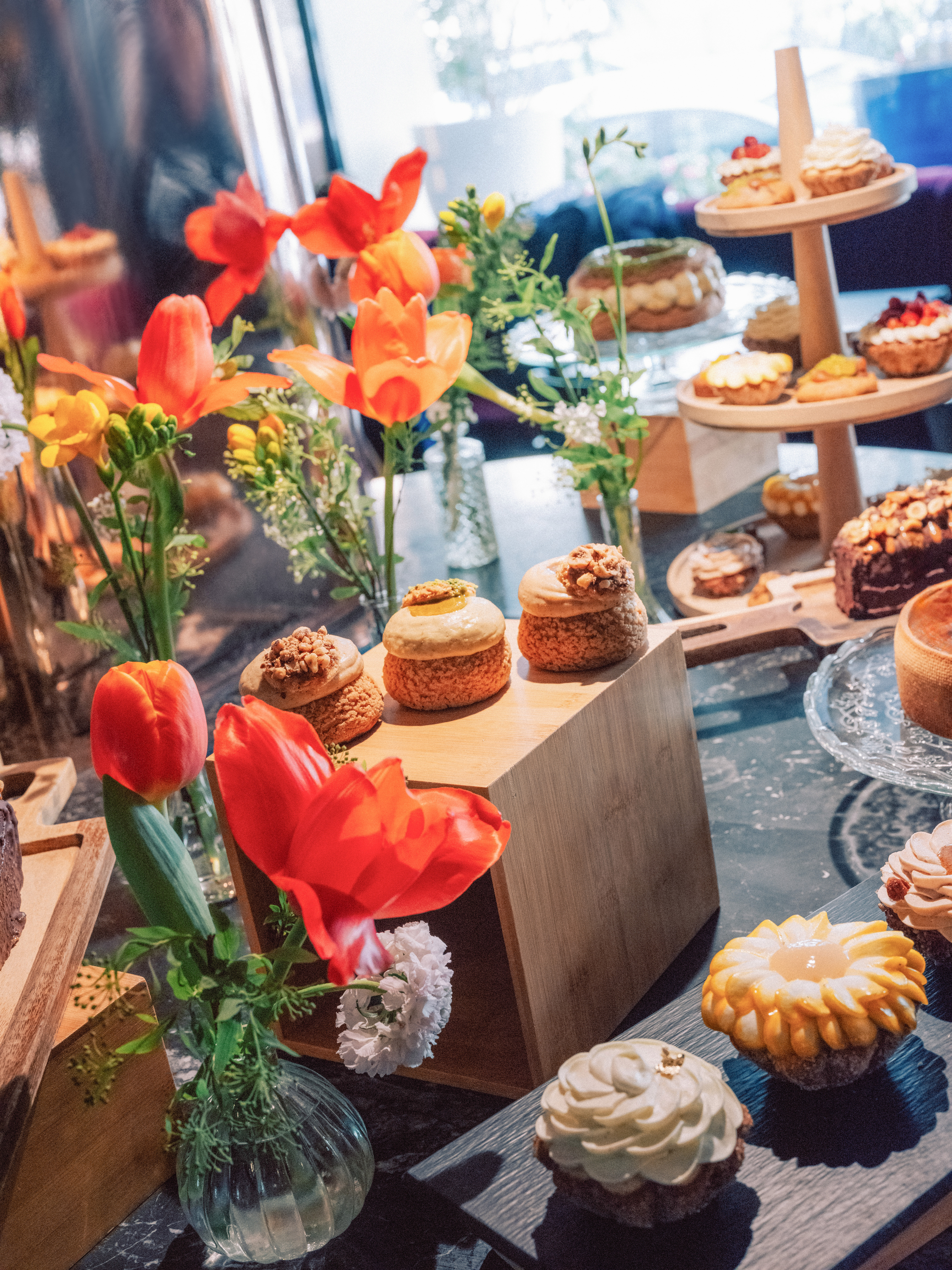 Gourmet dessert display with choux pastries, tarts, cakes, and red tulips.