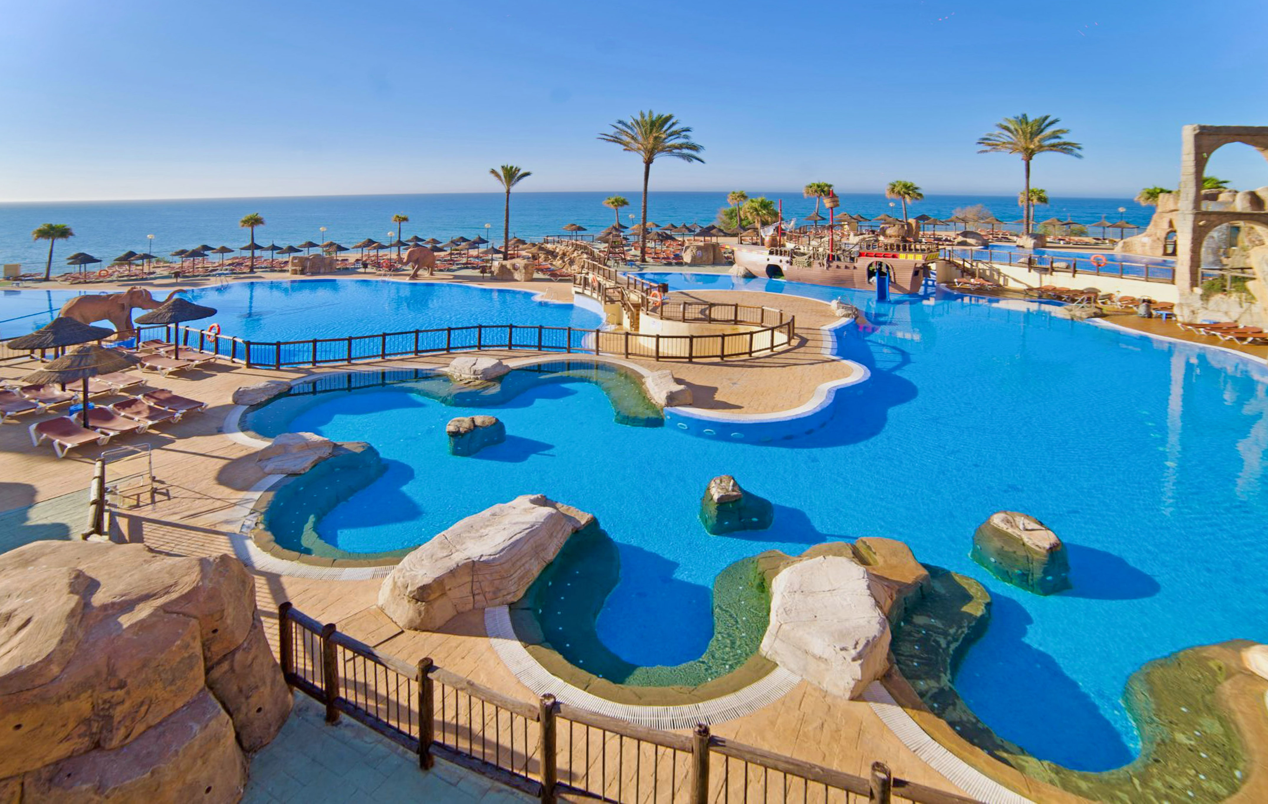 a large pool with a beach and palm trees