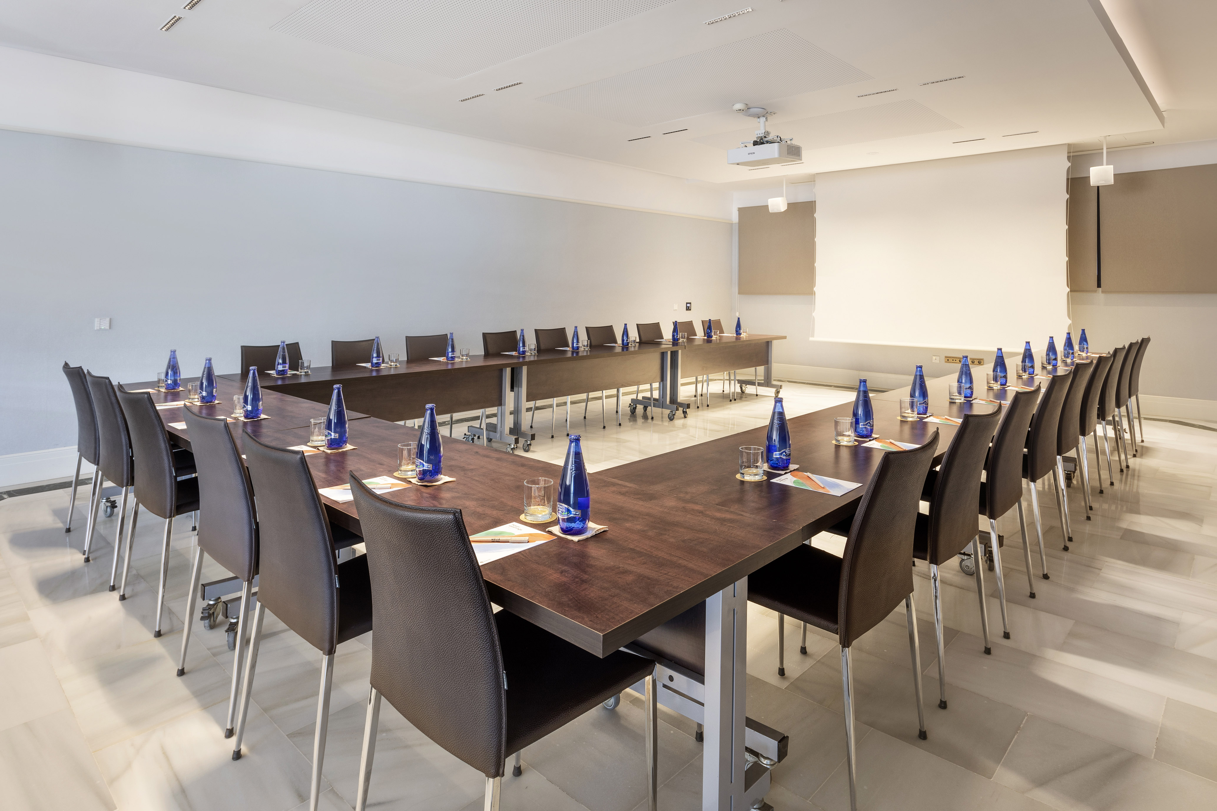 Modern U-shaped conference room with projector, chairs, and water bottles.