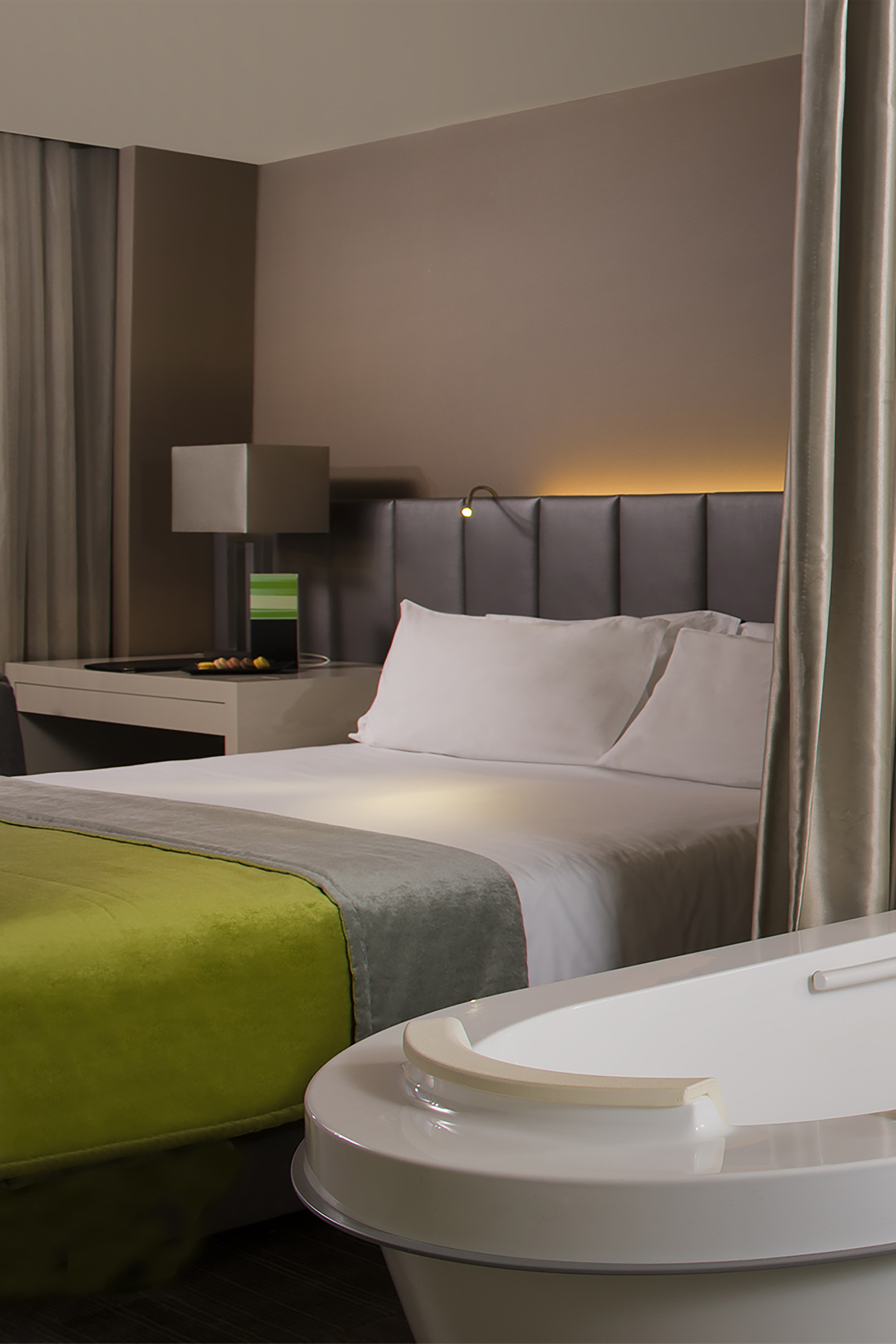 a bed with a green blanket and a white bathtub