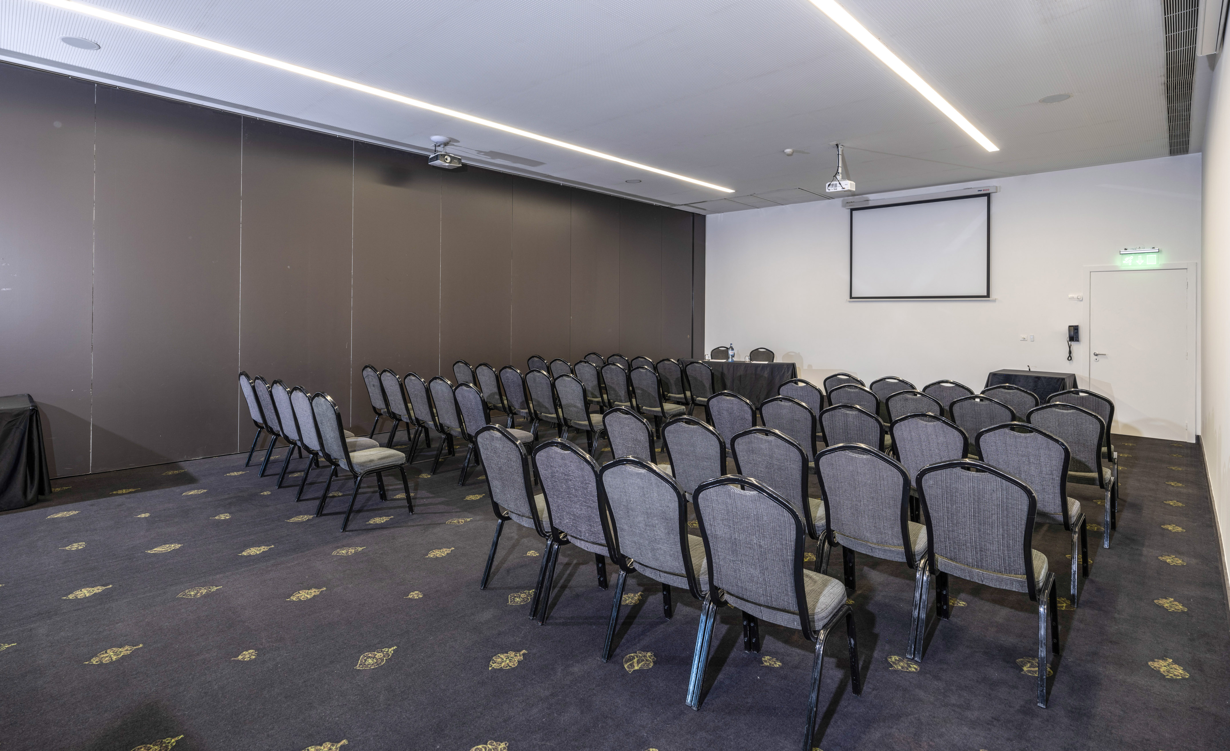Empty conference room with rows of gray chairs, projector screen, and dark carpet.