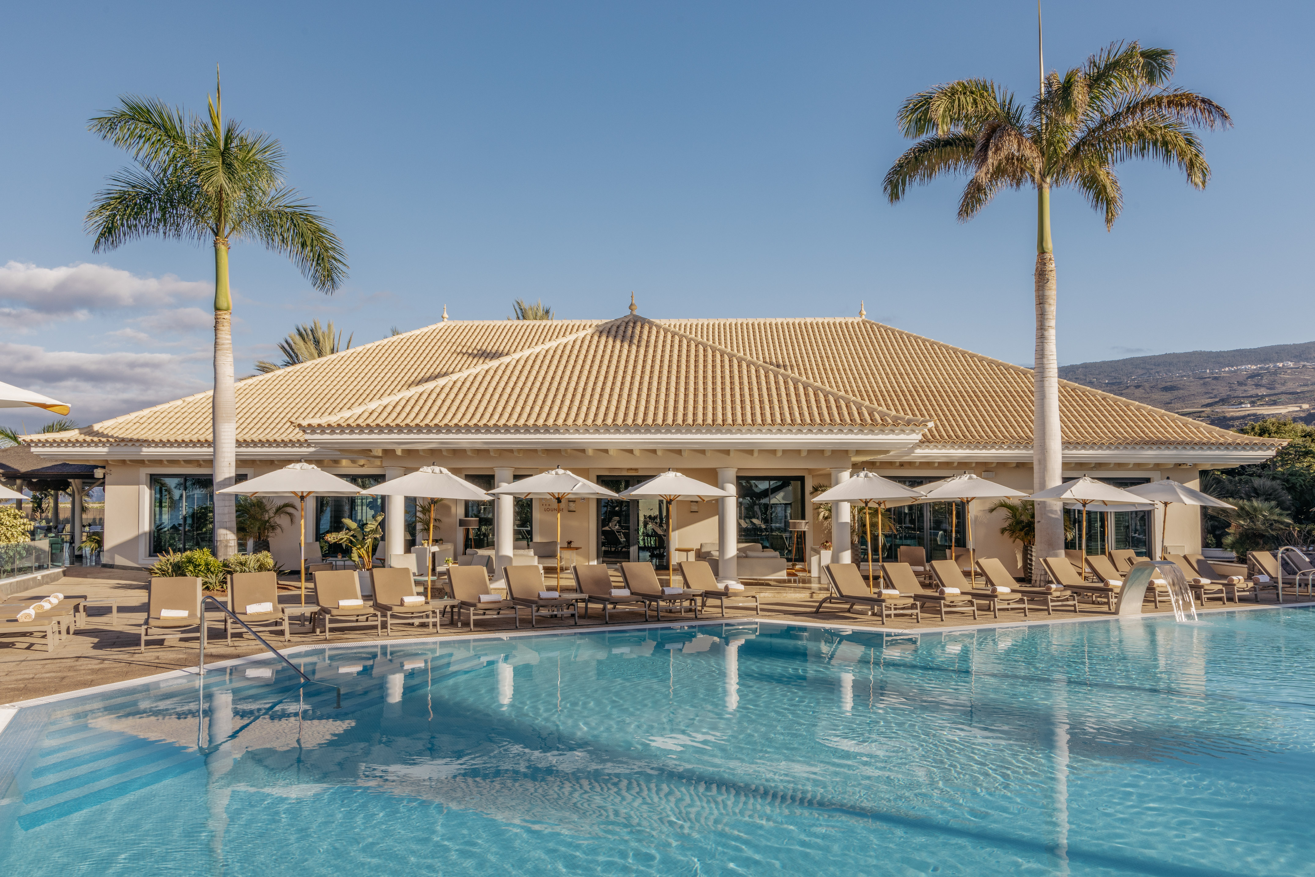 Resort pool, lounge chairs, umbrellas, palm trees, and hotel building.