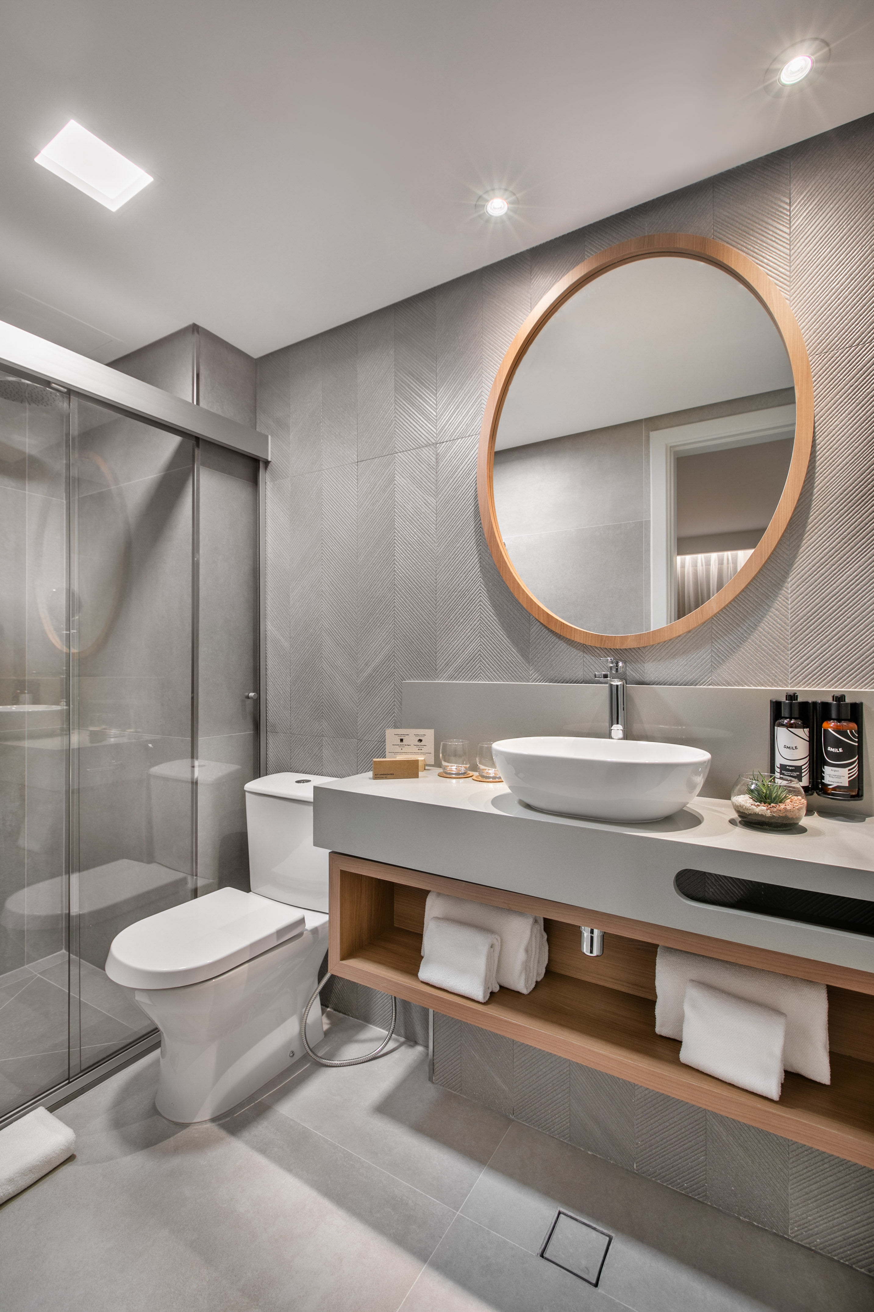 Modern gray bathroom with glass shower, vessel sink, and wooden mirror.