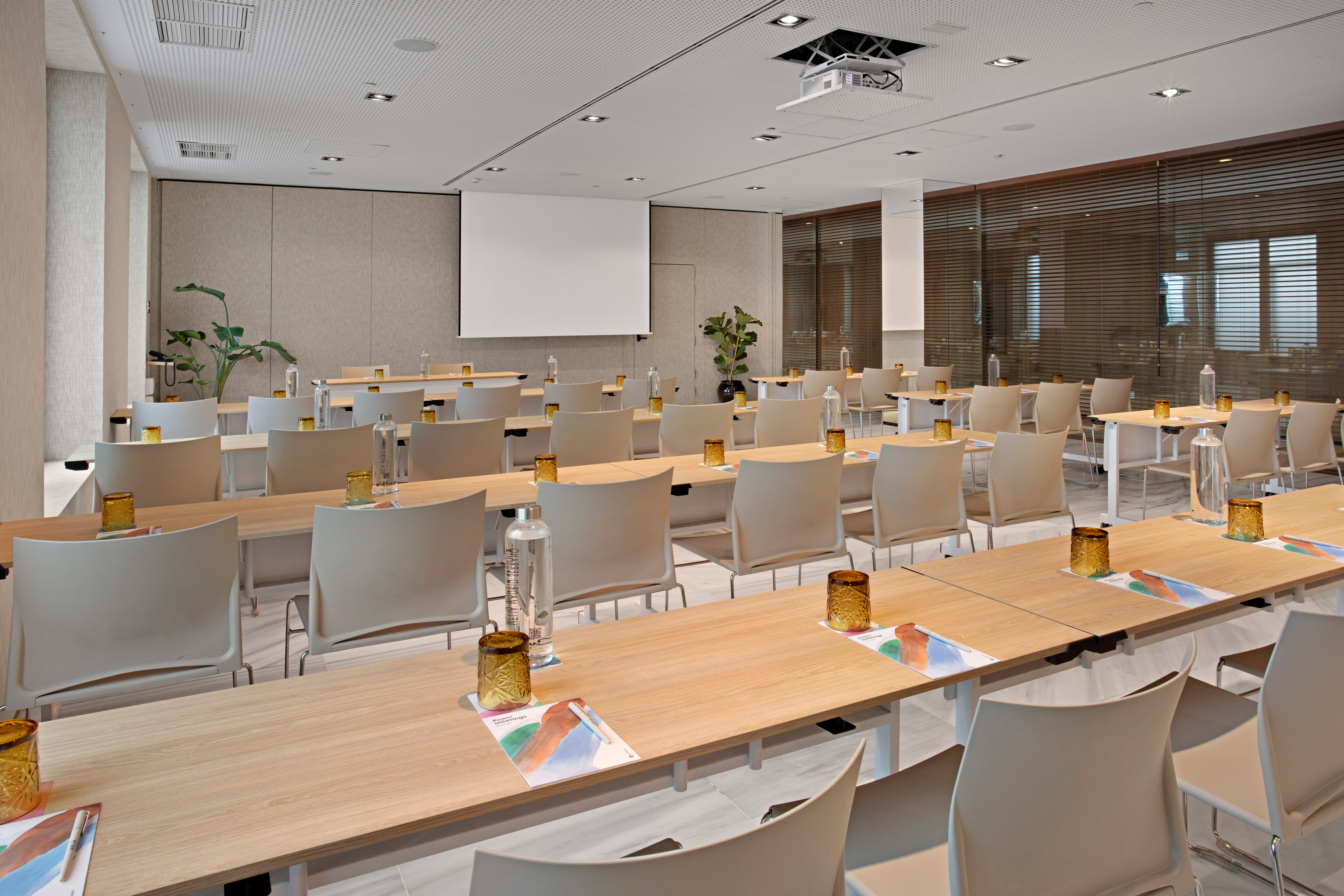 Modern meeting room with light wood tables, chairs, projector, and screen.