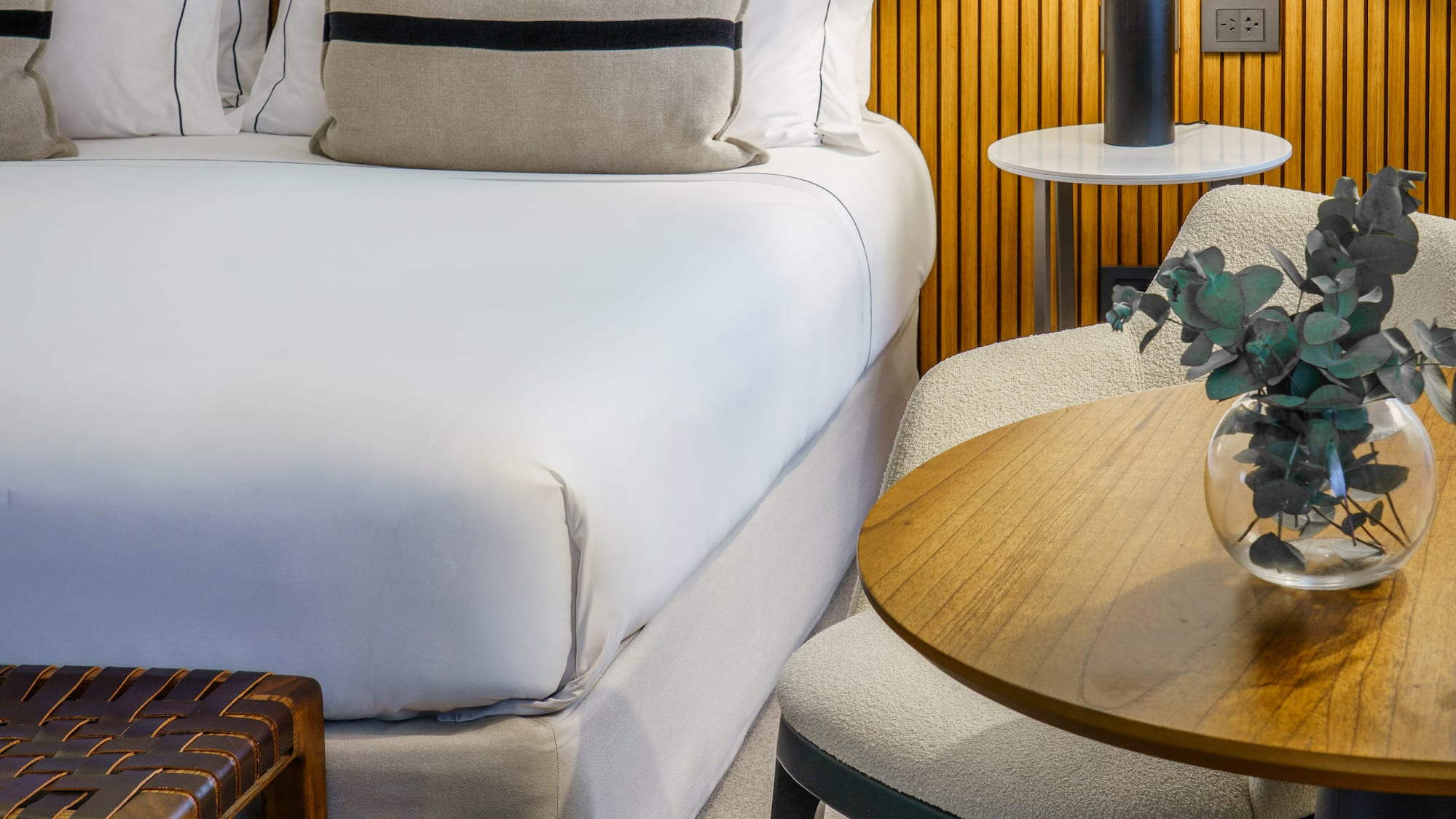 a bed with white sheets and pillows next to a table and lamp