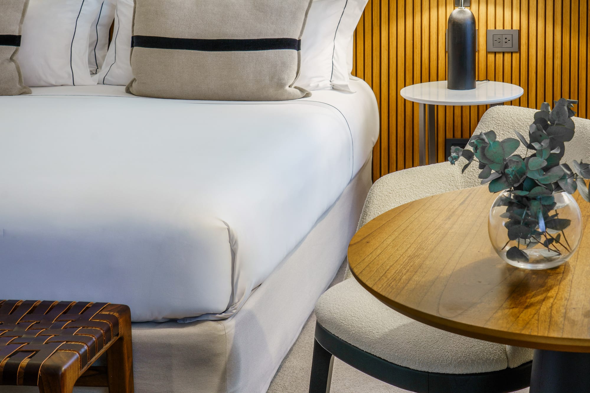 a bed with white sheets and pillows next to a table and lamp