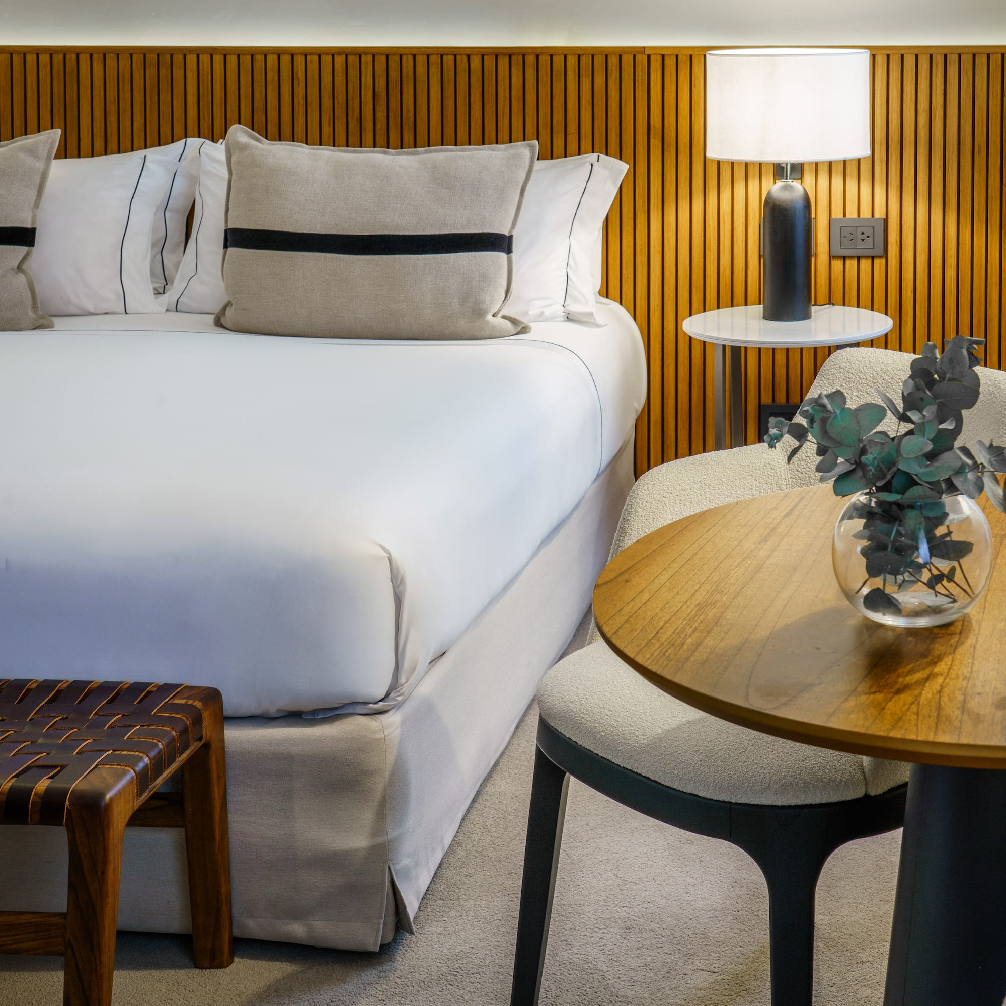 a bed with white sheets and pillows next to a table and lamp