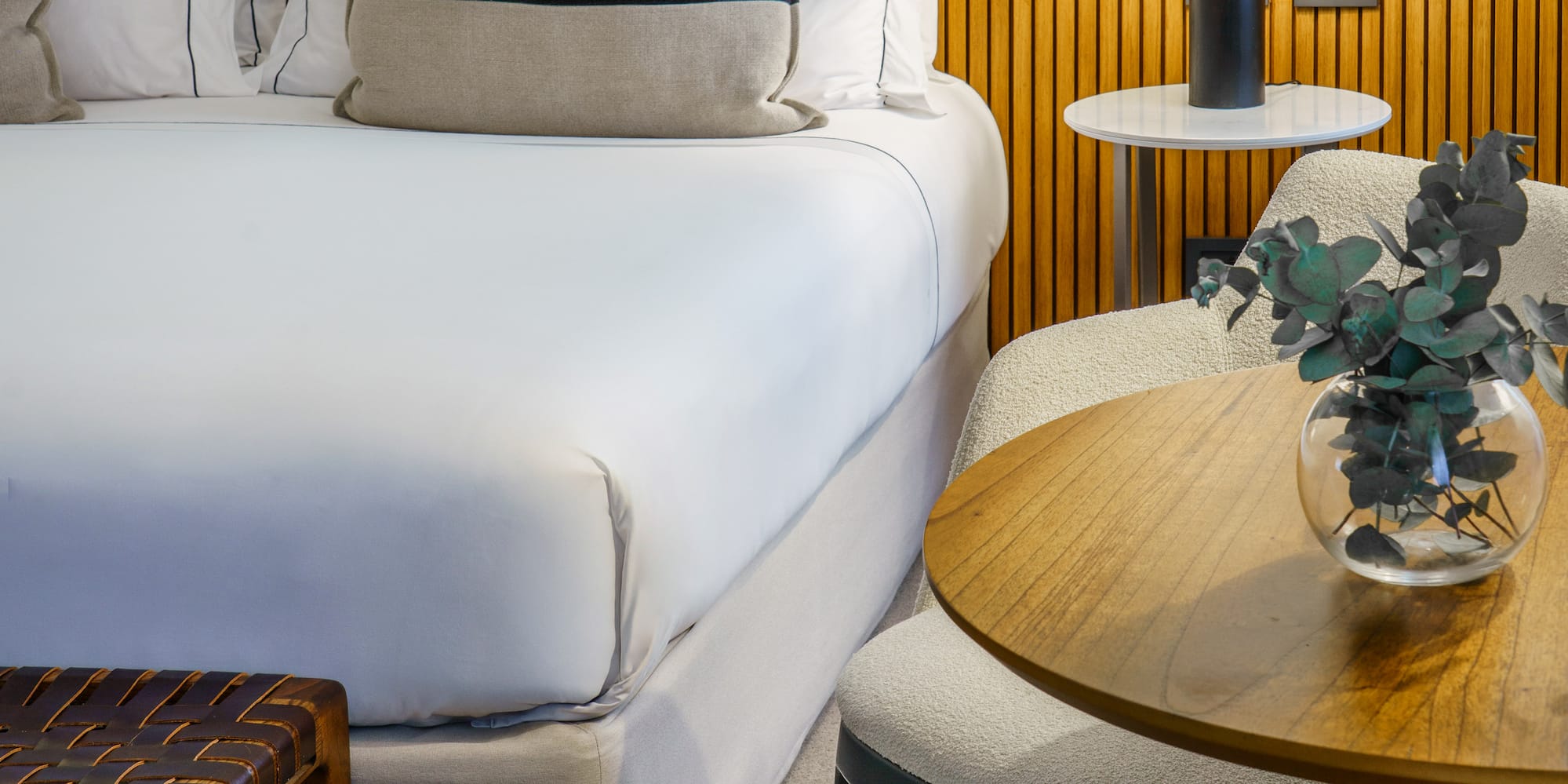 a bed with white sheets and pillows next to a table and lamp