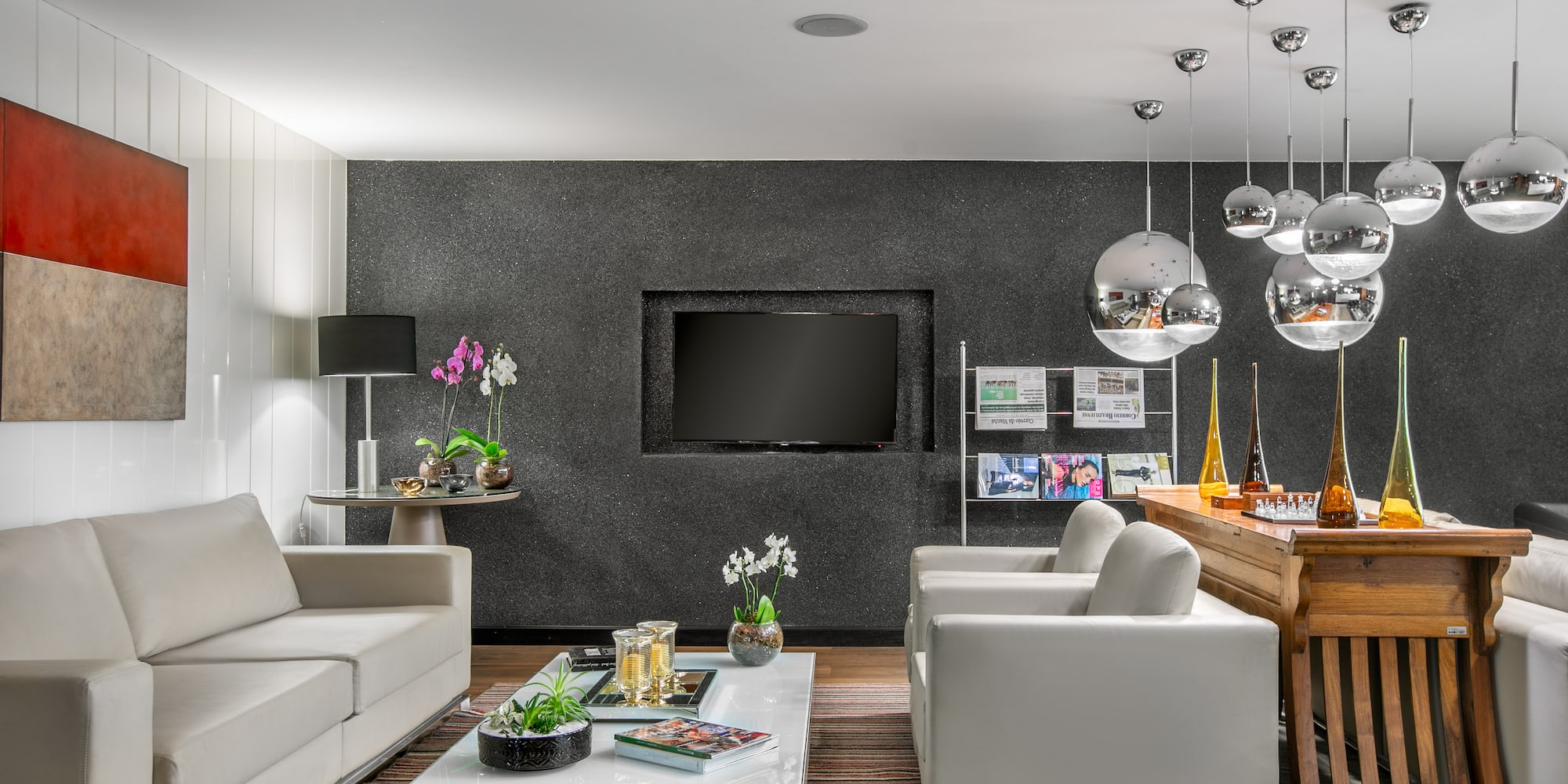 Modern living room: white sofas, dark wall, recessed TV, chrome pendant lights.