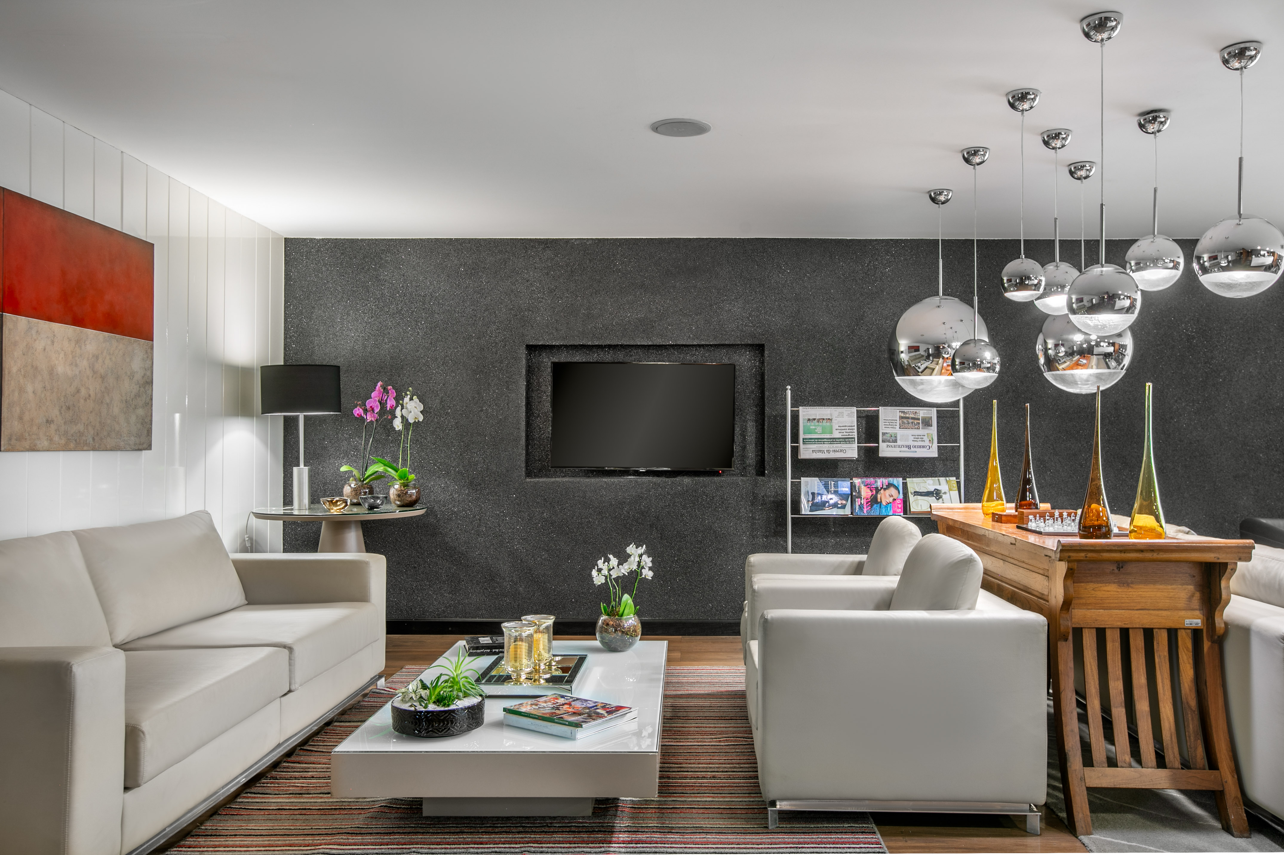 Modern living room: white sofas, dark wall, recessed TV, chrome pendant lights.