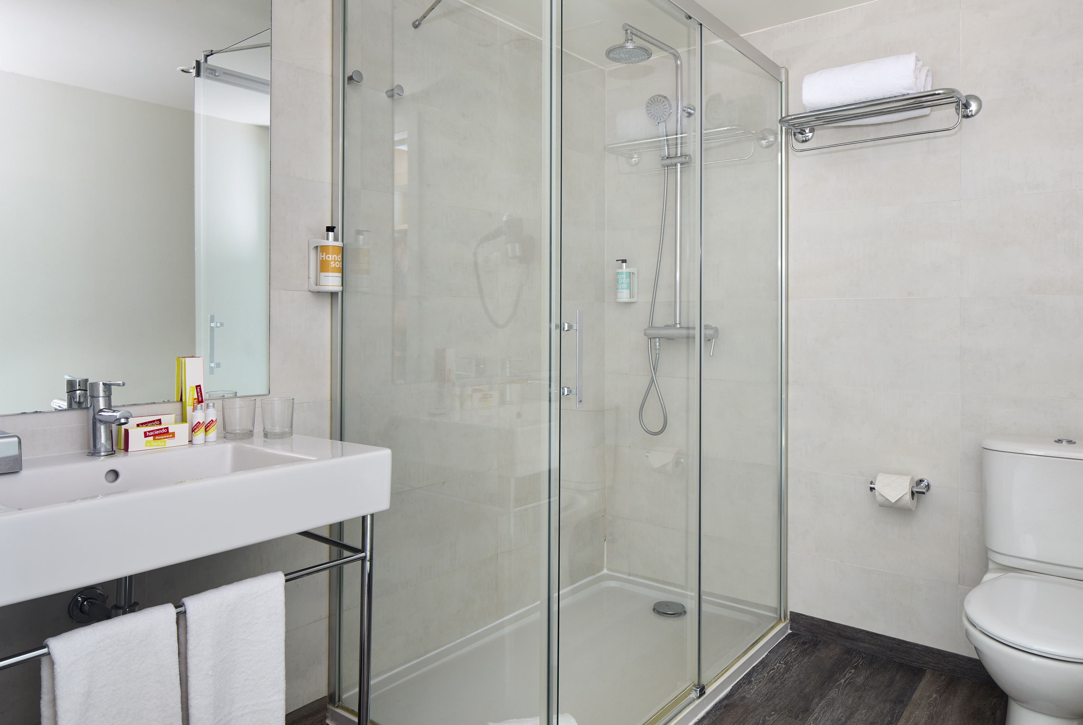 Modern hotel bathroom with walk-in shower, white sink, and toilet.