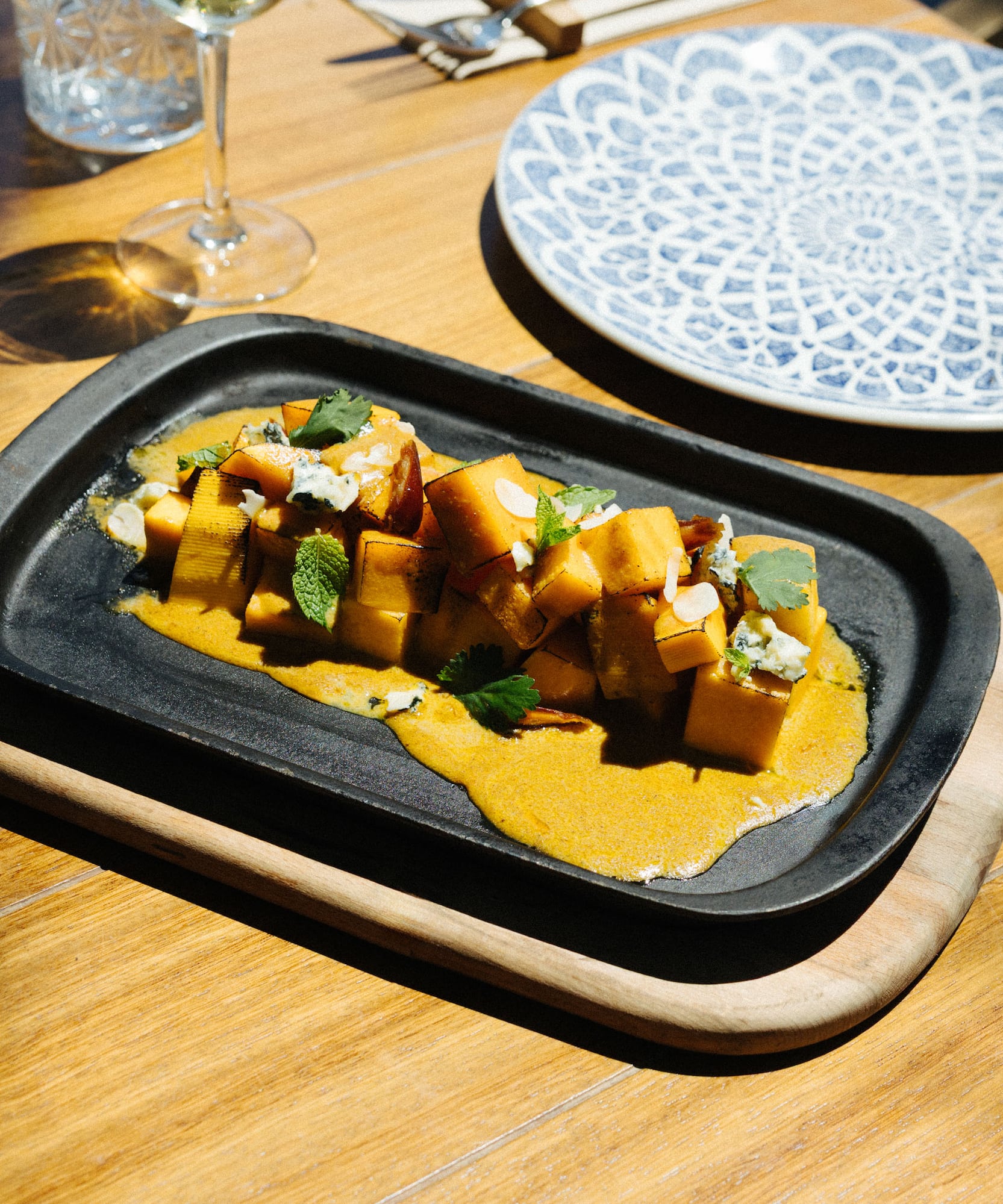 Gourmet roasted squash with yellow sauce, mint, cheese on a black skillet.