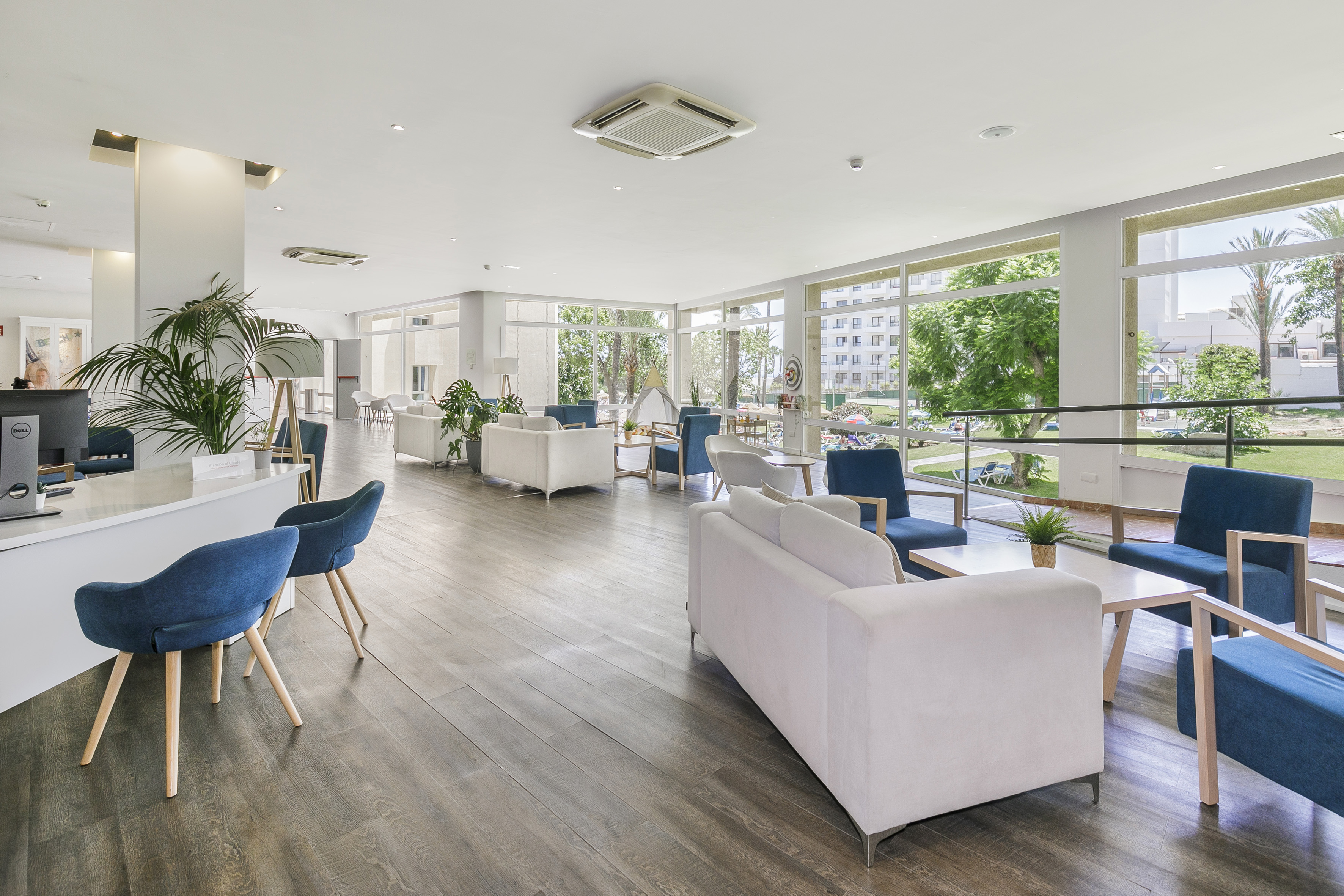 Hotel reception area with modern seating, white desk, and bright garden views.