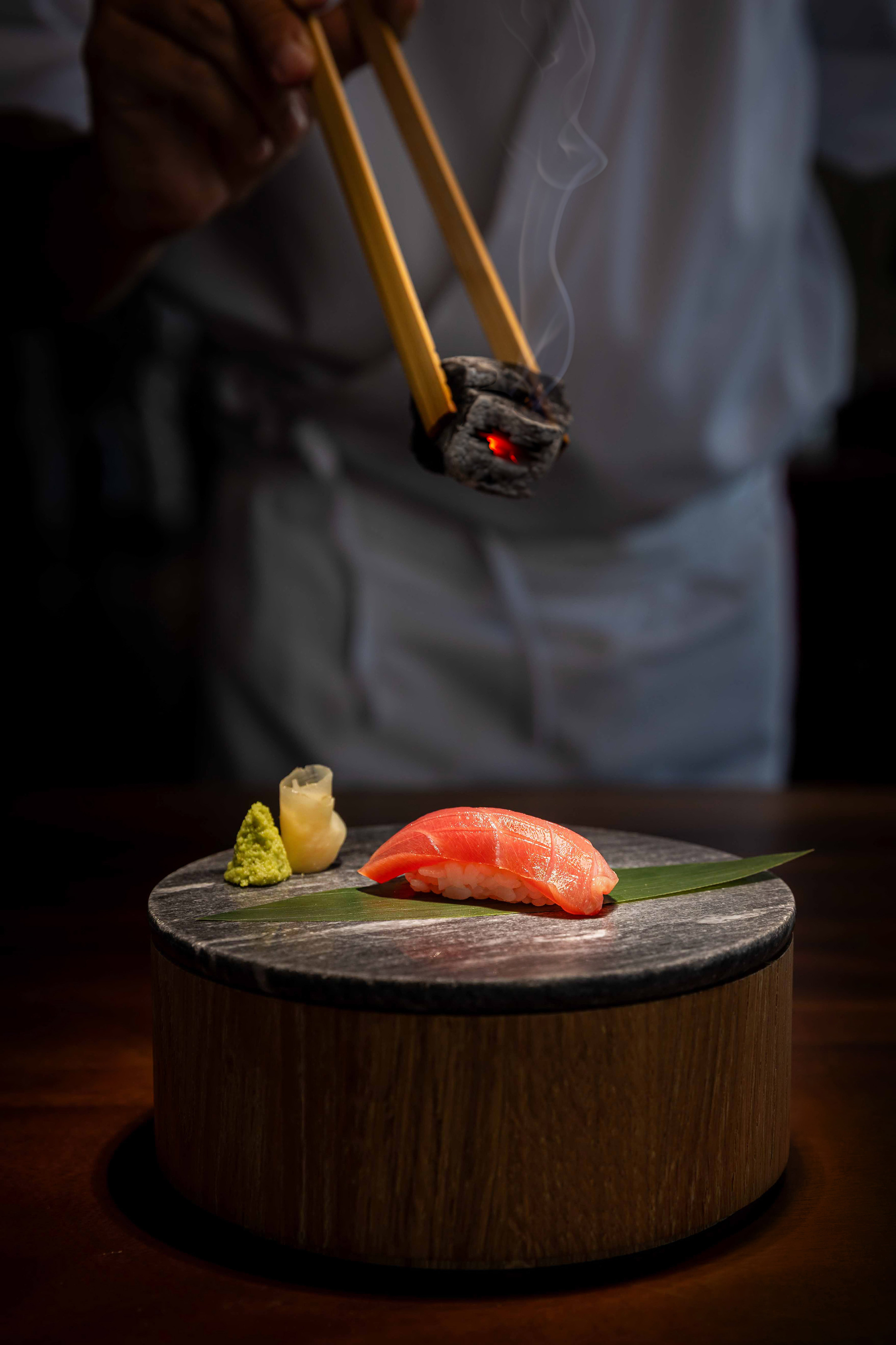 Chef searing tuna nigiri sushi with smoking charcoal on a stone plate.