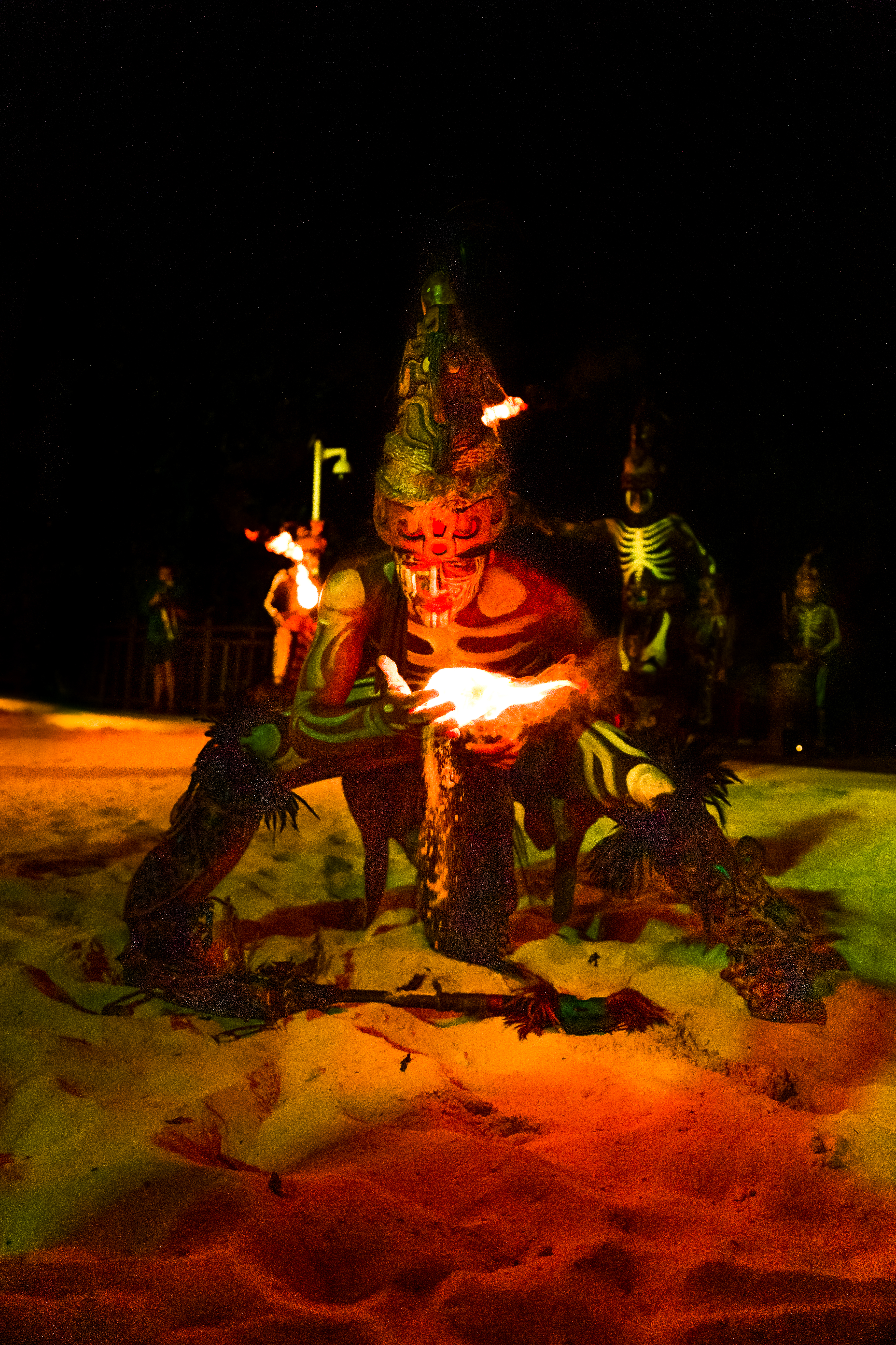 Fire dancer in tribal costume and skeleton paint holding flames at night.
