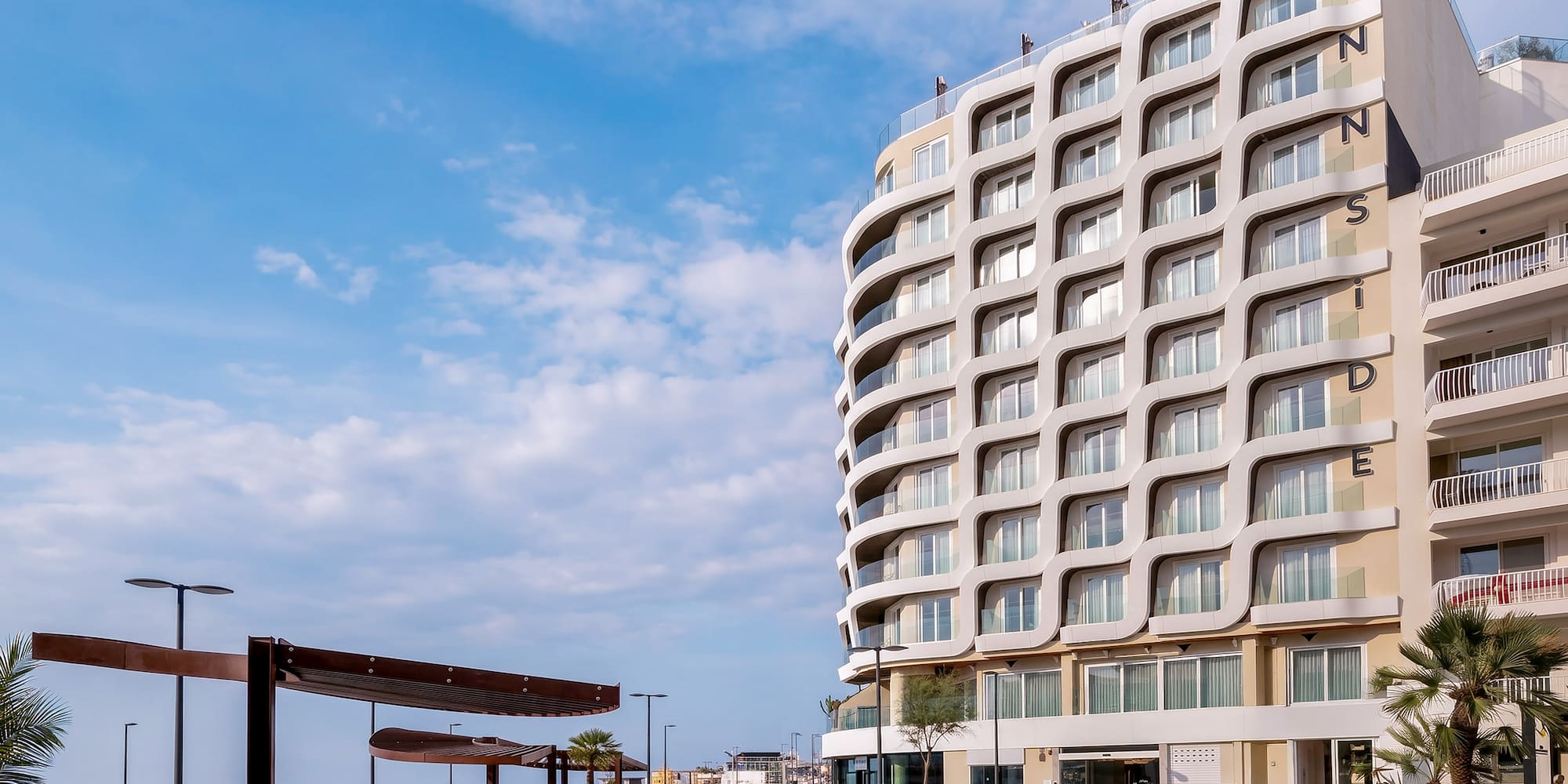 INNSiDE hotel with wavy facade overlooking a sunny seaside promenade.