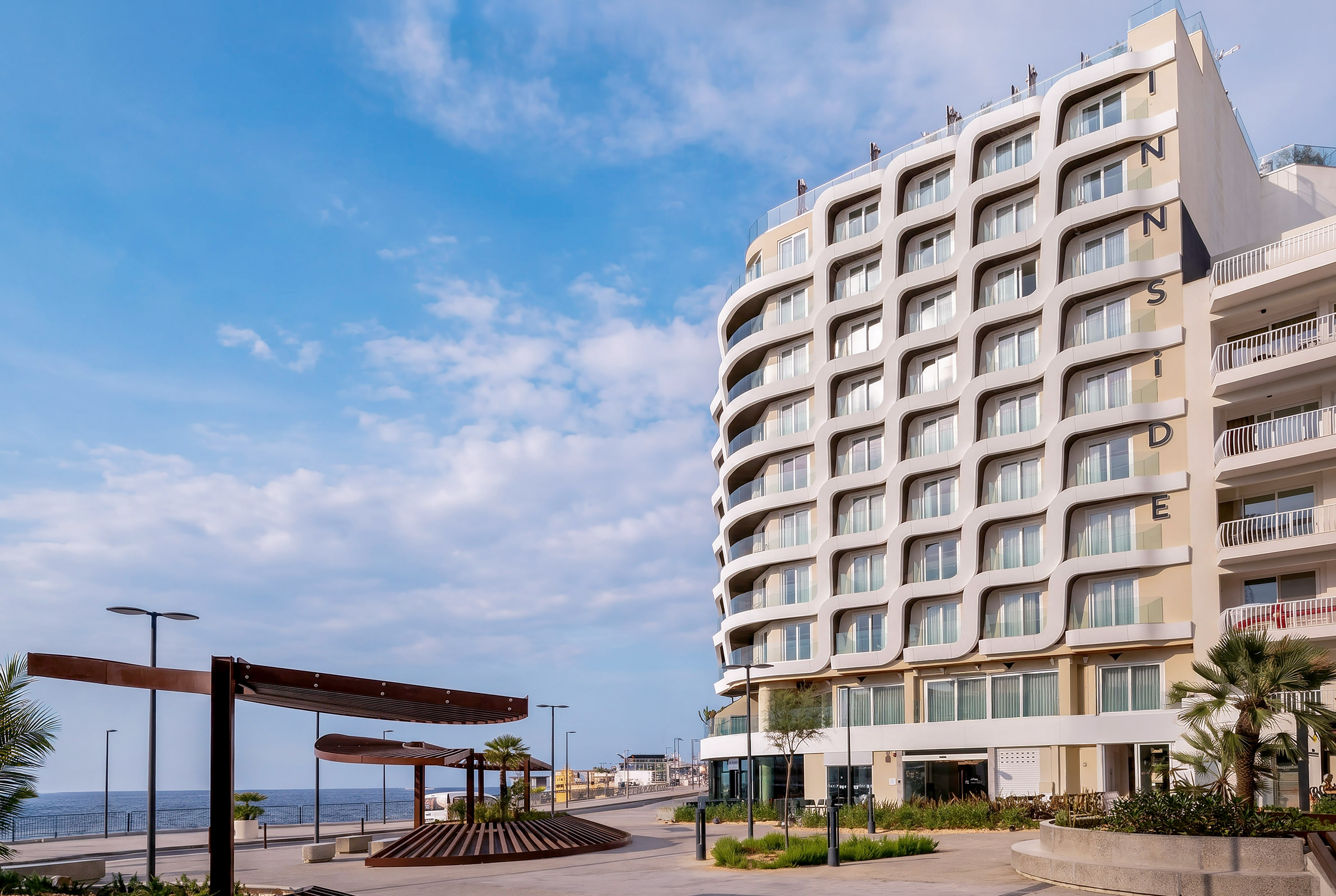 INNSiDE hotel with wavy facade overlooking a sunny seaside promenade.