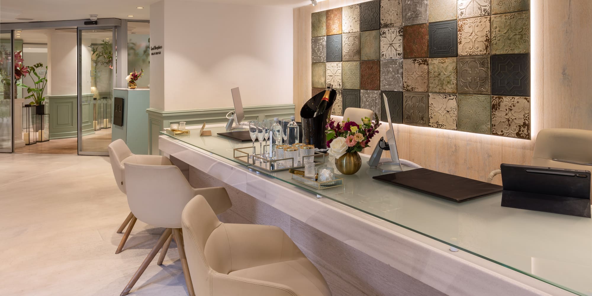Hotel reception desk with champagne, flowers, and unique patterned wall tiles.