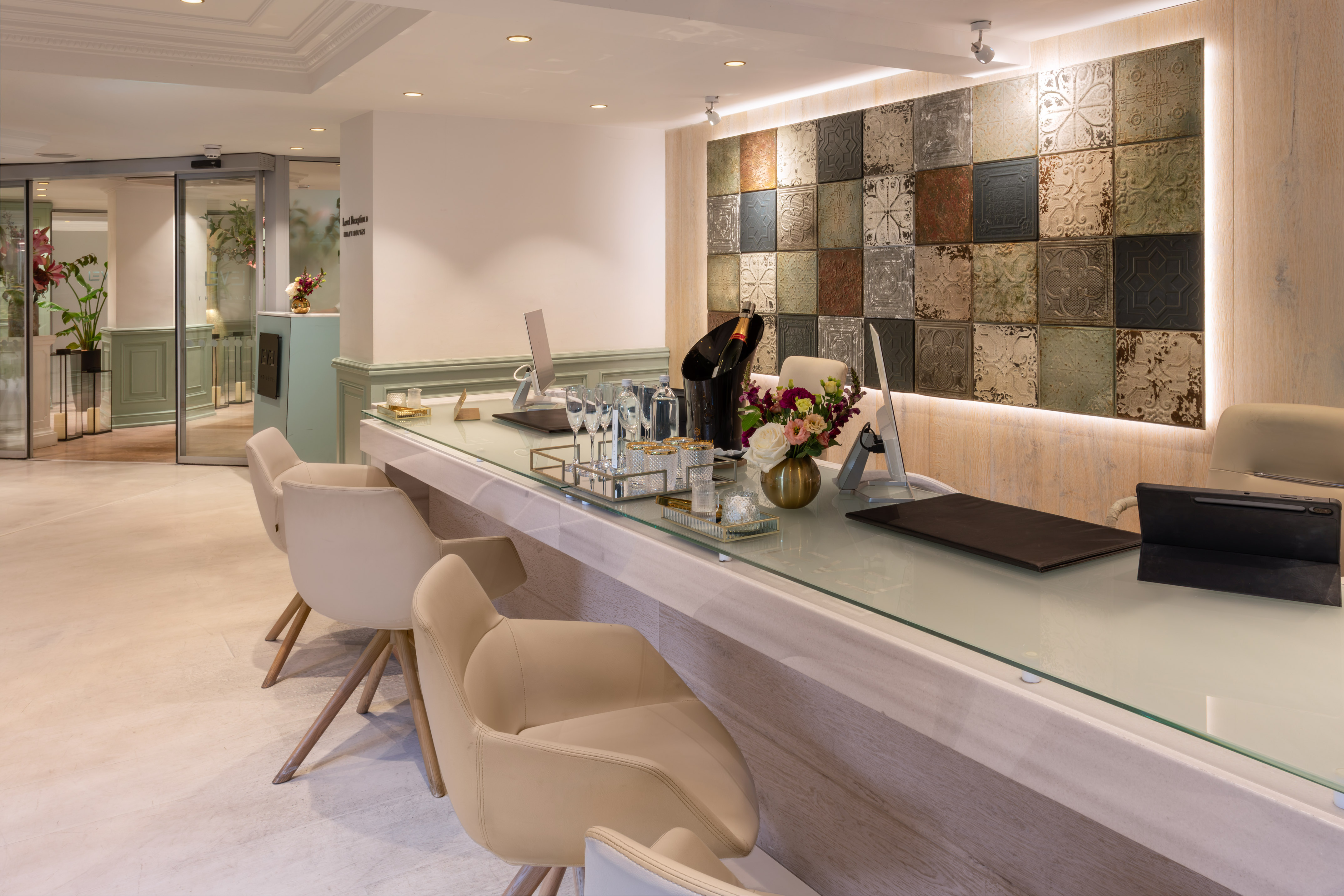 Hotel reception desk with champagne, flowers, and unique patterned wall tiles.