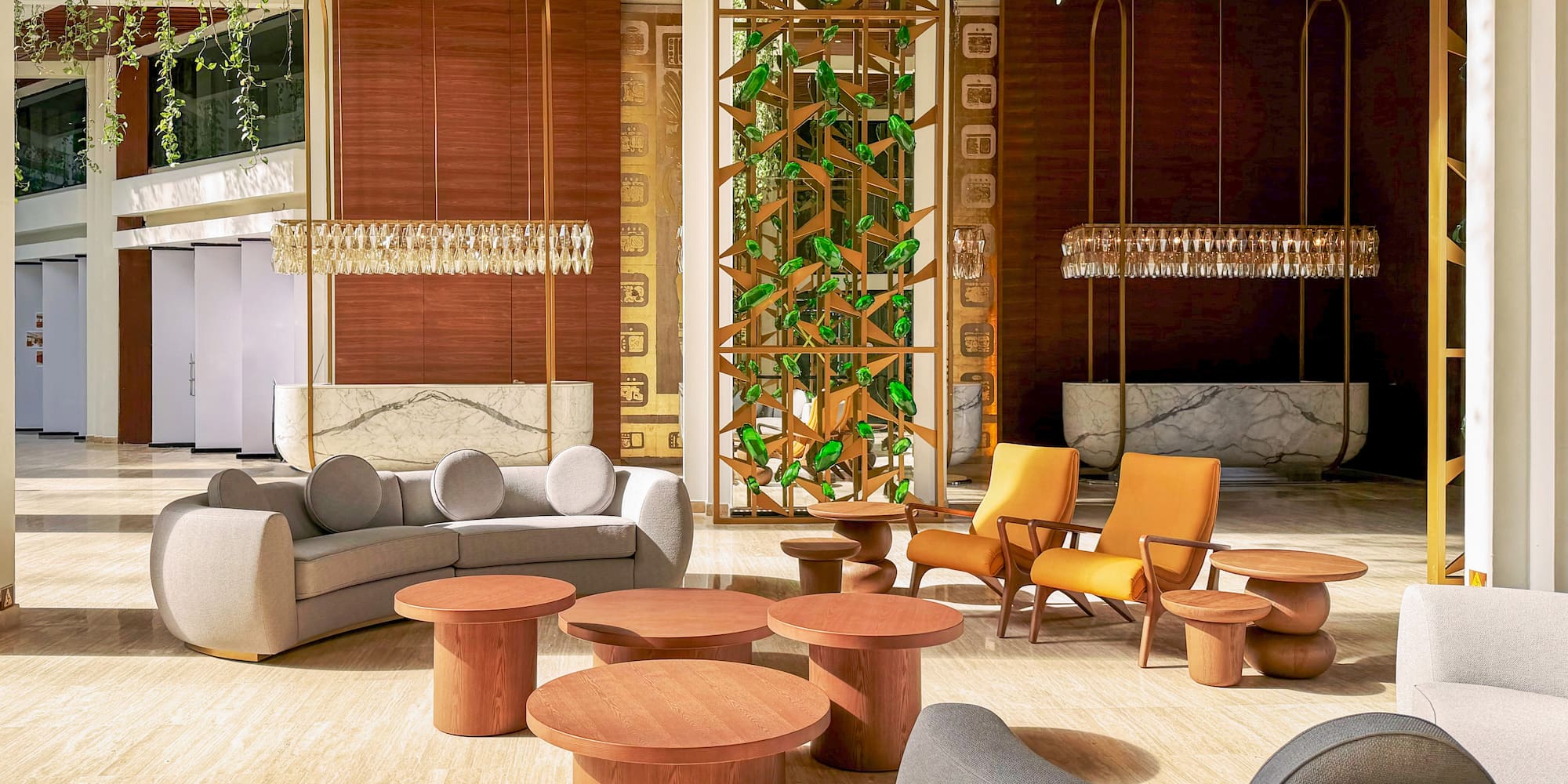 Modern hotel lobby lounge with sofa, orange chairs, wood tables, and green plants.