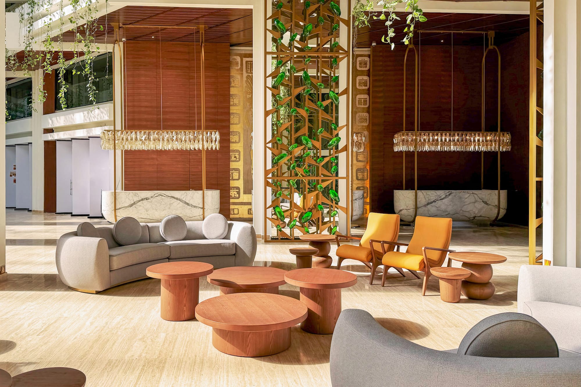 Modern hotel lobby lounge with sofa, orange chairs, wood tables, and green plants.