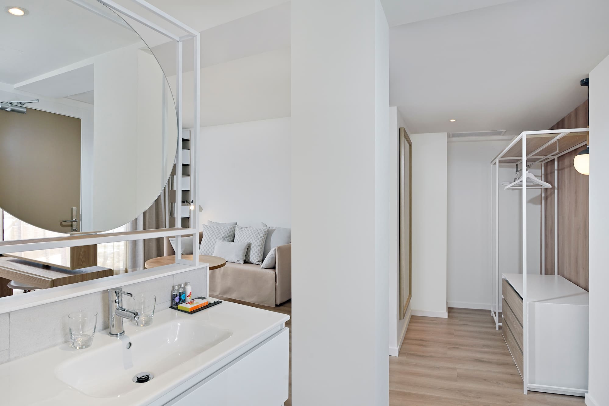 Modern open-plan suite with bathroom vanity, living area, and open closet.