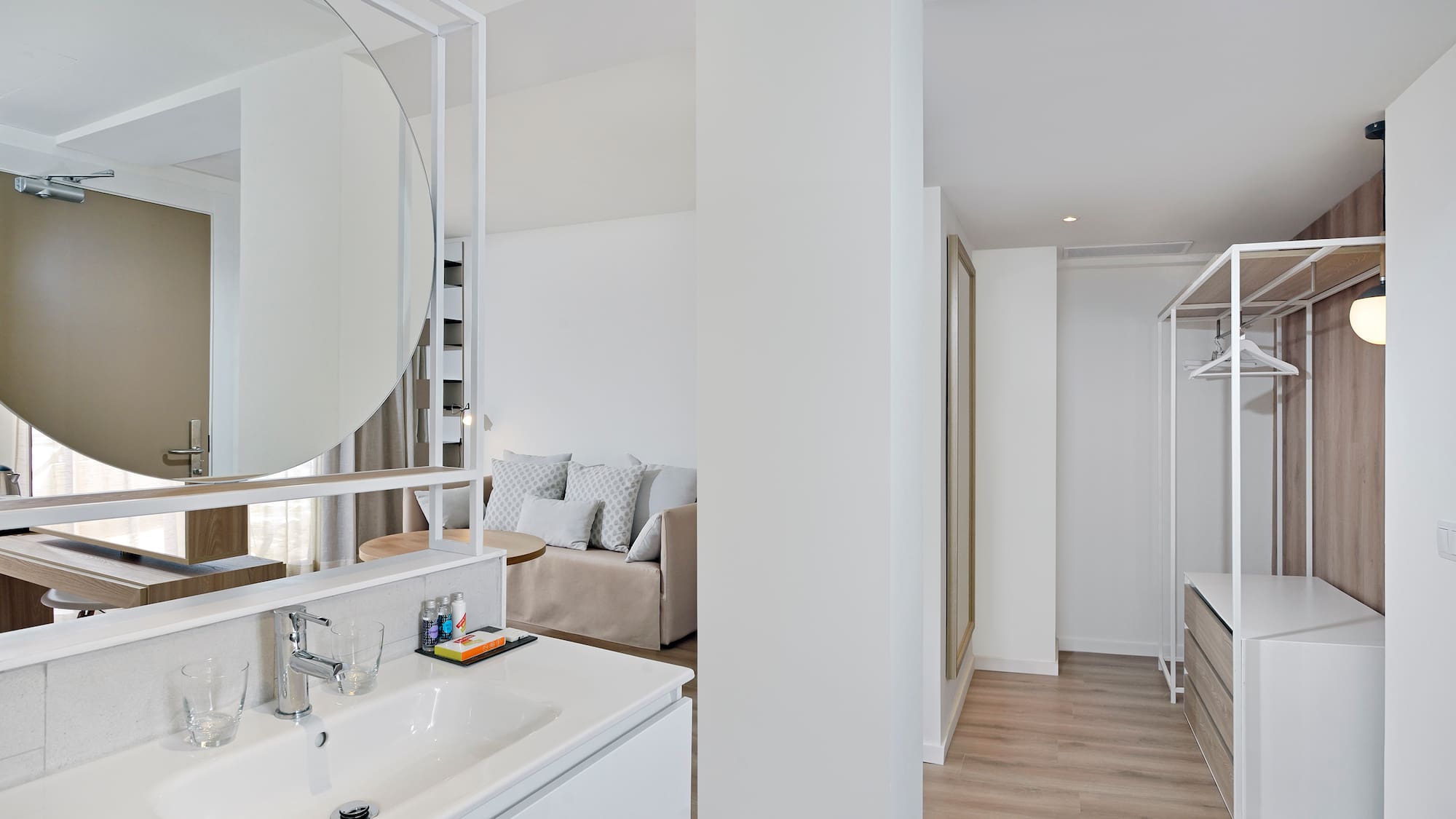 Modern open-plan suite with bathroom vanity, living area, and open closet.