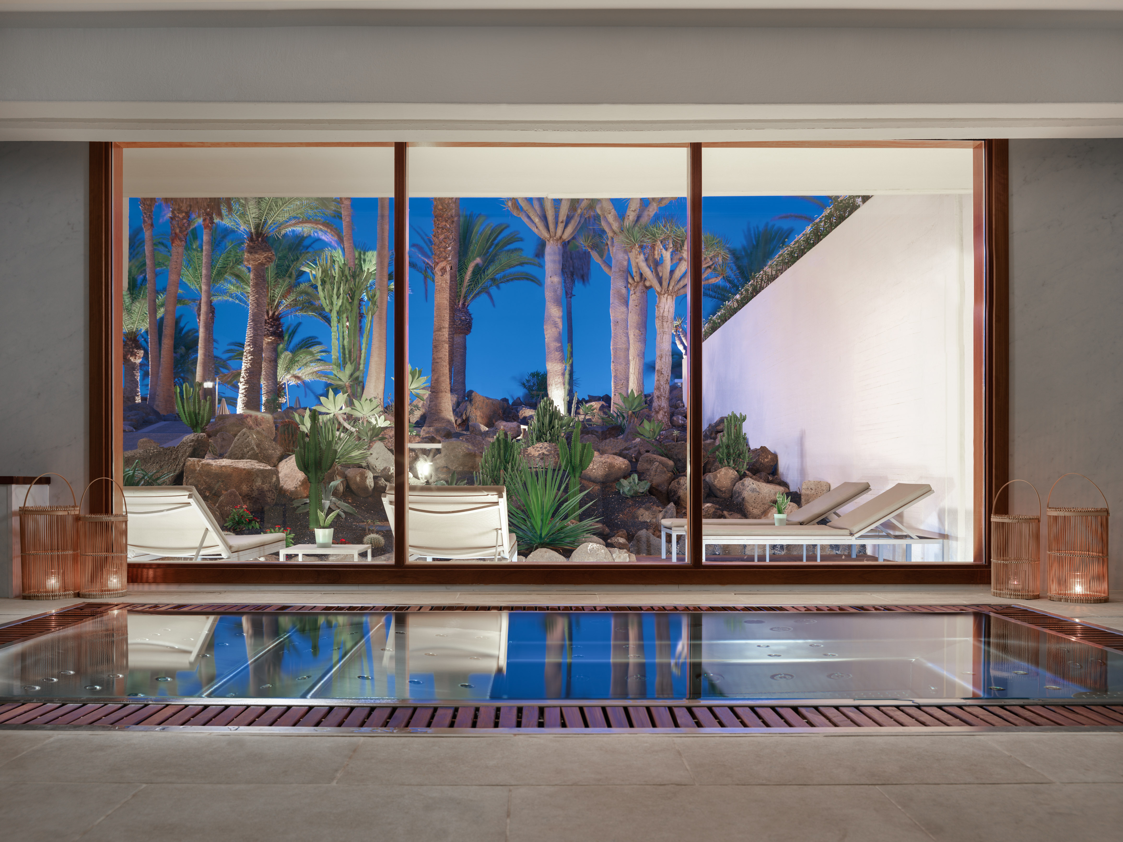 Luxury indoor spa pool with tropical palm garden view at night.