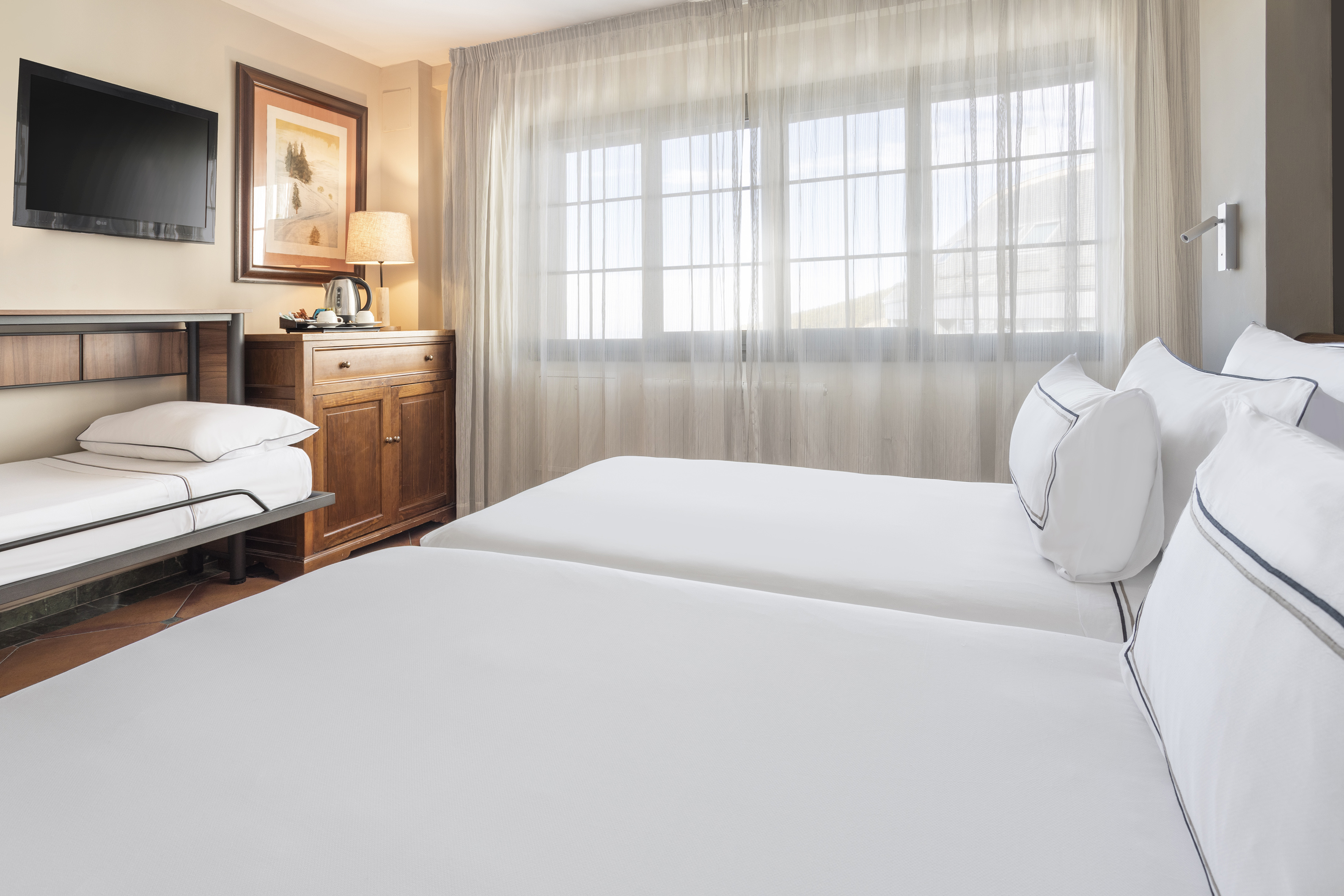 Bright hotel room with two twin beds, extra bed, TV, and sheer window.