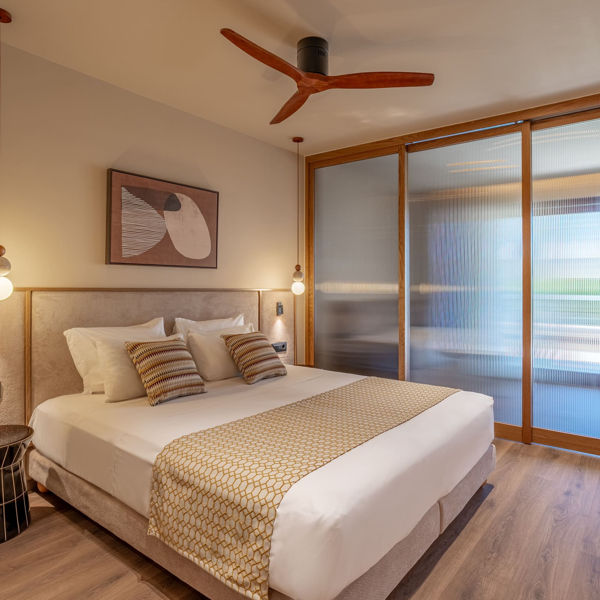 Modern hotel room with king bed, wooden ceiling fan, and fluted glass doors.