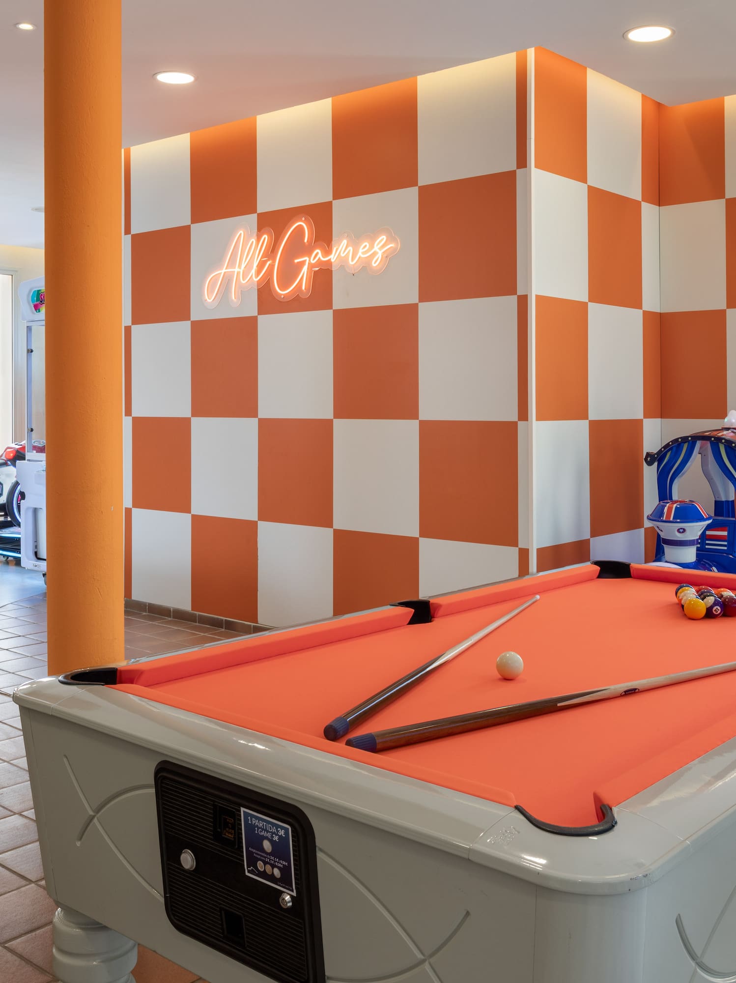 Sala de juegos moderna con billar naranja, futbolín y letrero neón "All Games".