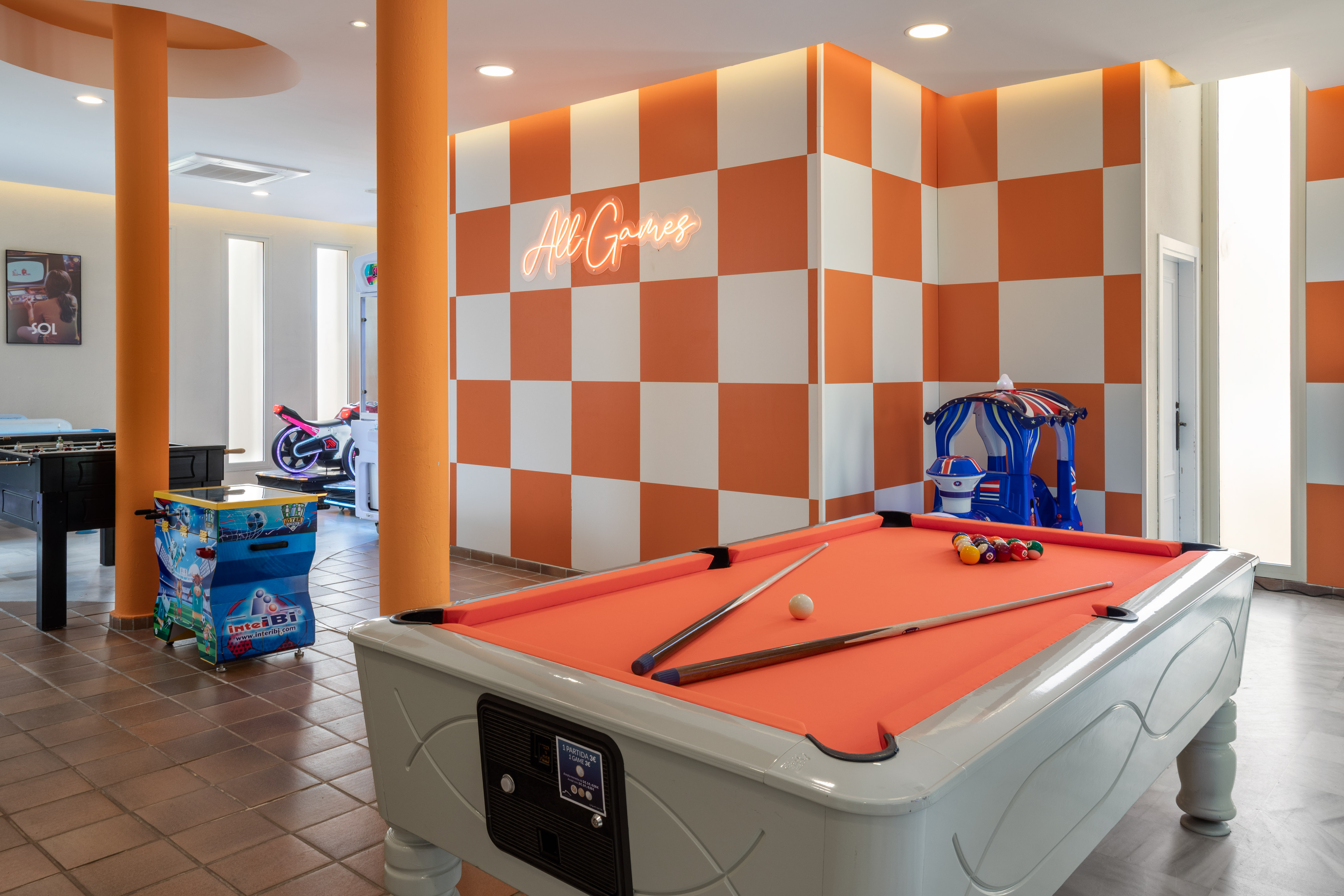 Sala de juegos moderna con billar naranja, futbolín y letrero neón "All Games".