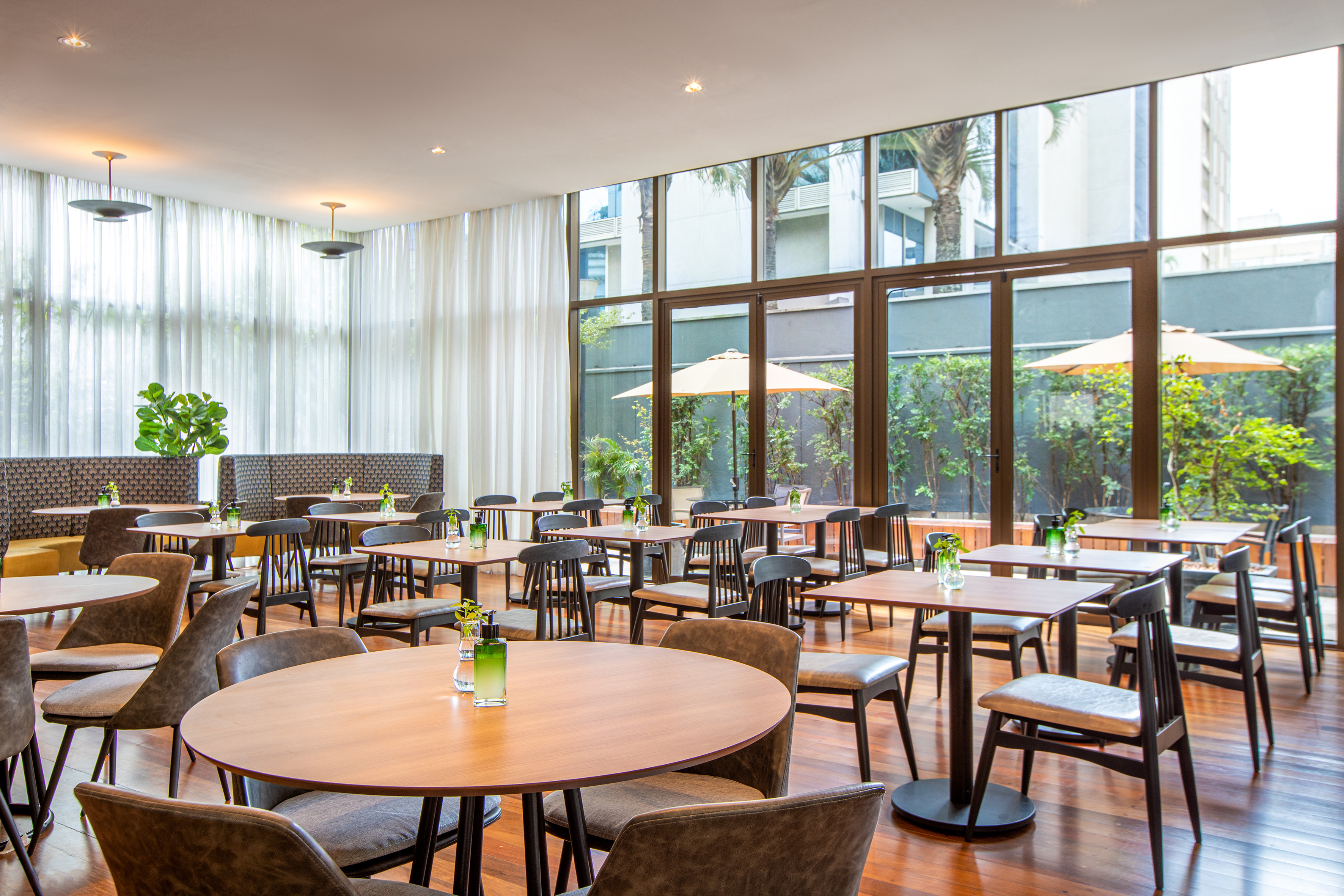 Modern restaurant, wooden tables, chairs, large windows facing garden.