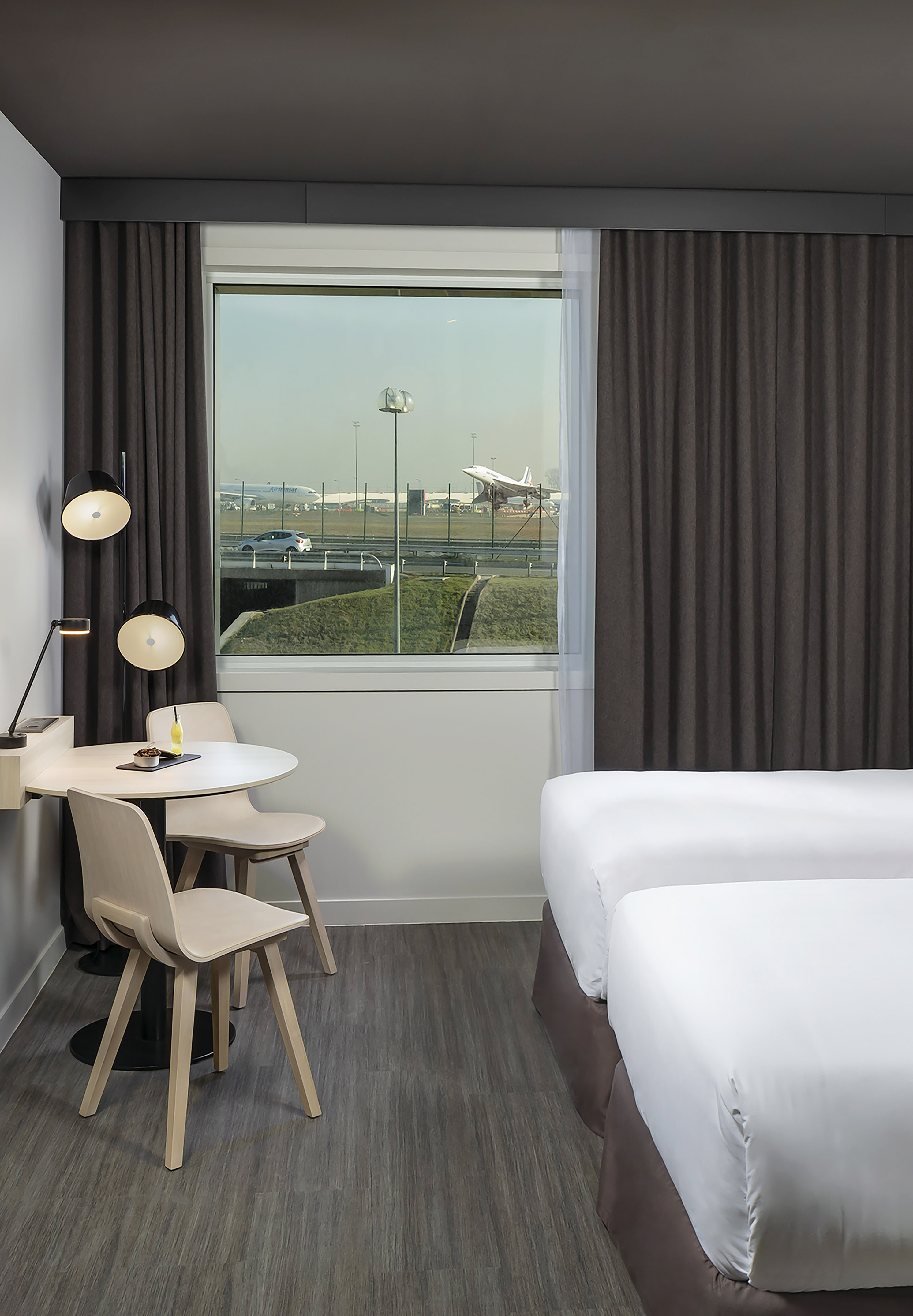 Airport hotel room with twin beds, modern table, and window view of planes on runway.