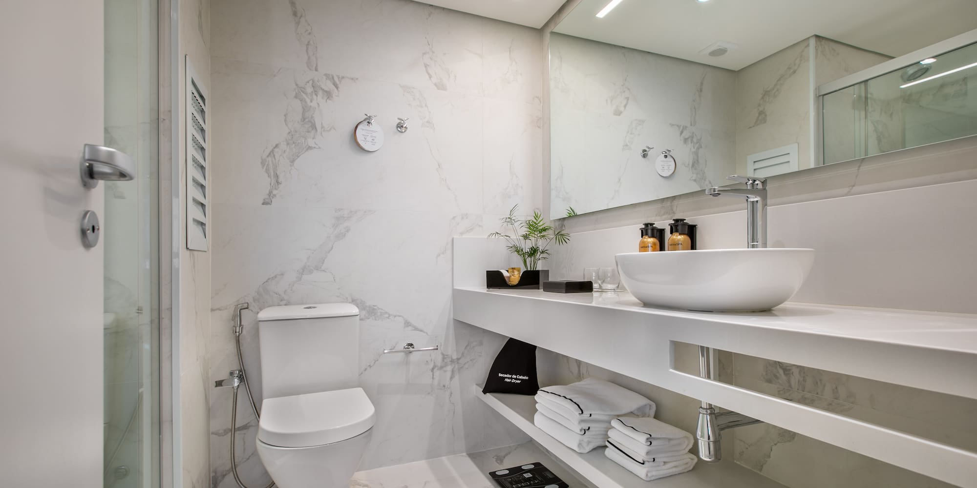 Modern white marble bathroom with a sleek vanity, toilet, and glass shower.