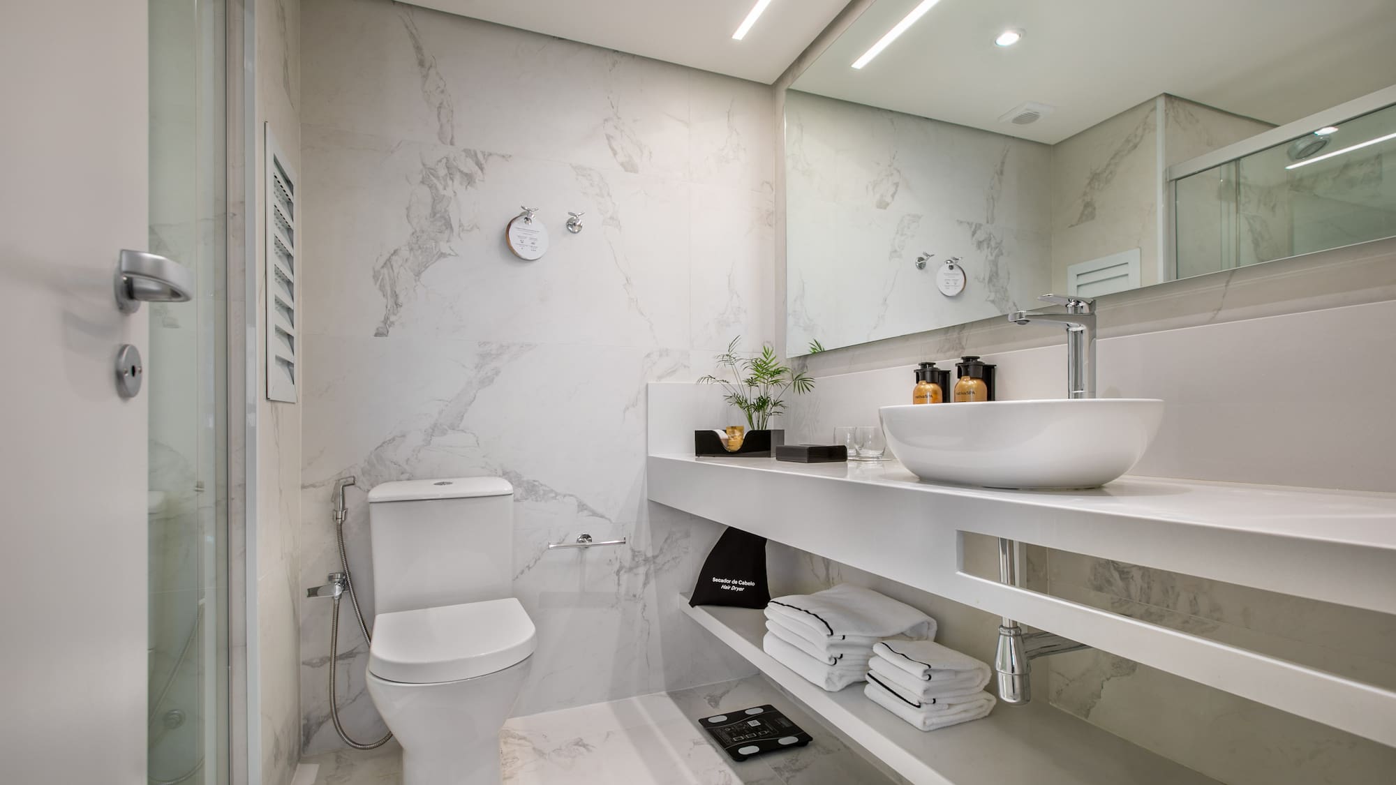 Modern white marble bathroom with a sleek vanity, toilet, and glass shower.