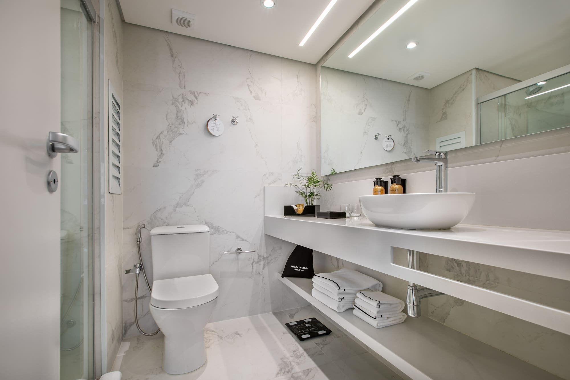 Sleek white marble bathroom with modern toilet, glass shower, and vanity sink.