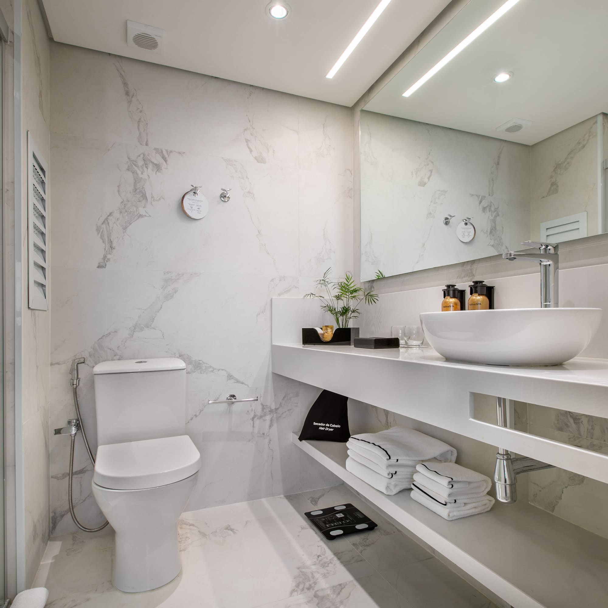 Sleek white marble bathroom with modern toilet, glass shower, and vanity sink.