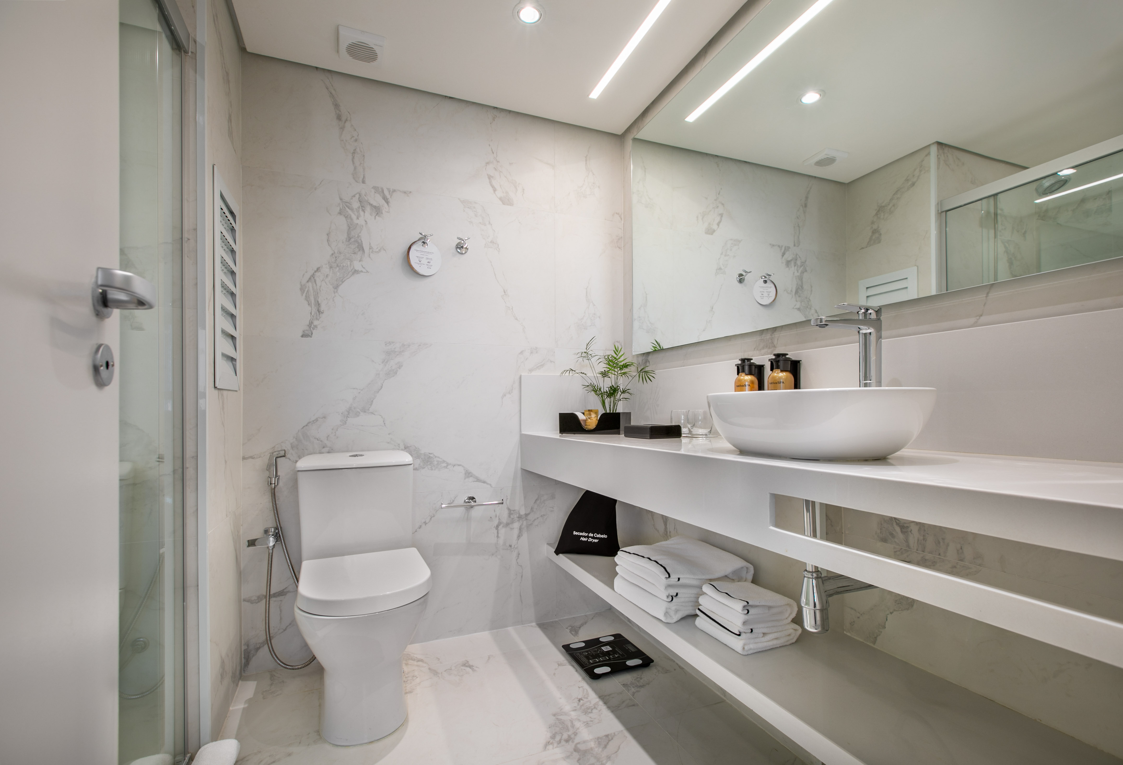 Sleek white marble bathroom with modern toilet, glass shower, and vanity sink.