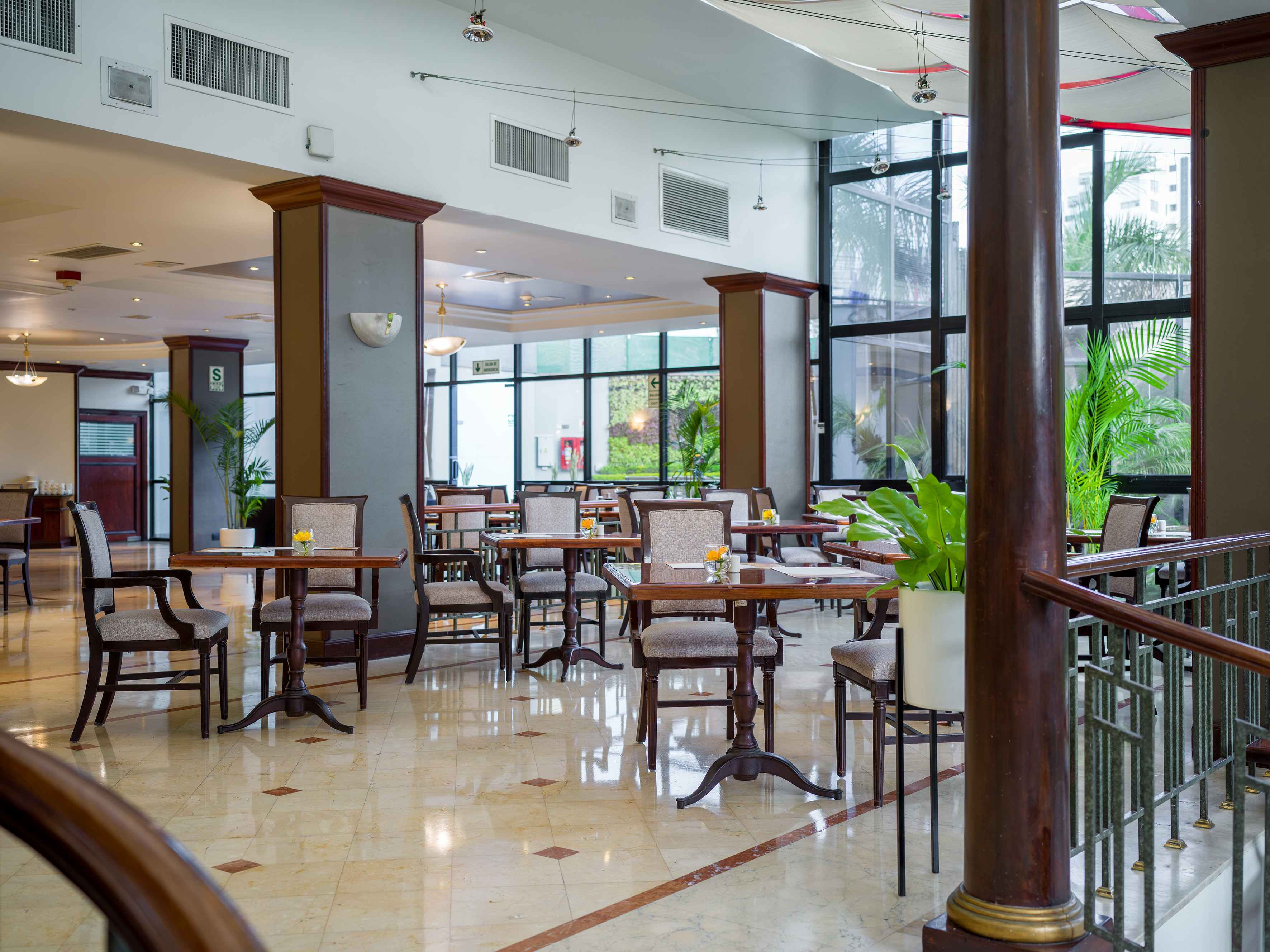Hotel restaurant interior with dining tables, marble floor, and large windows.