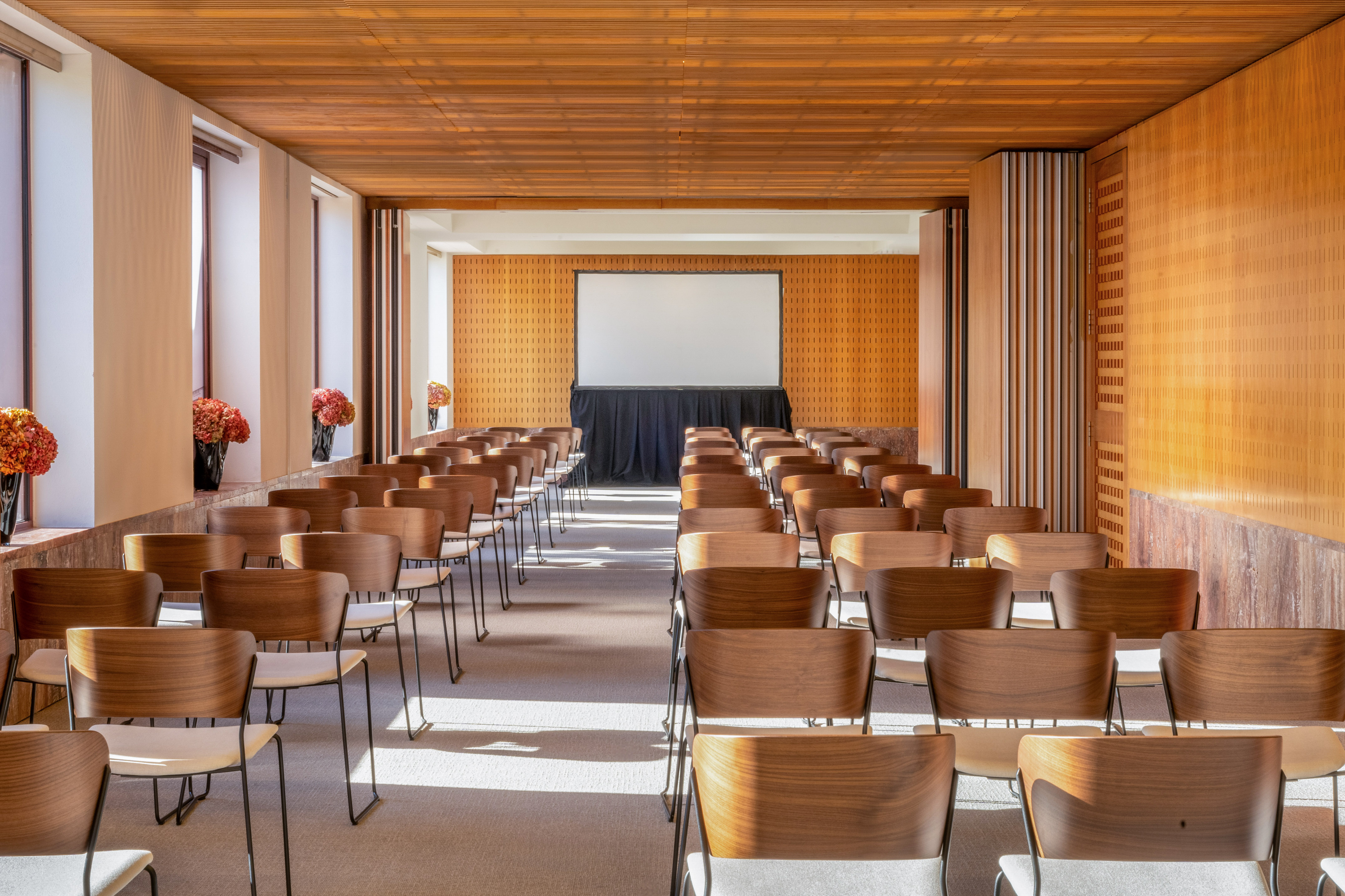 Conference room with rows of empty chairs, presentation screen, and wood interior.