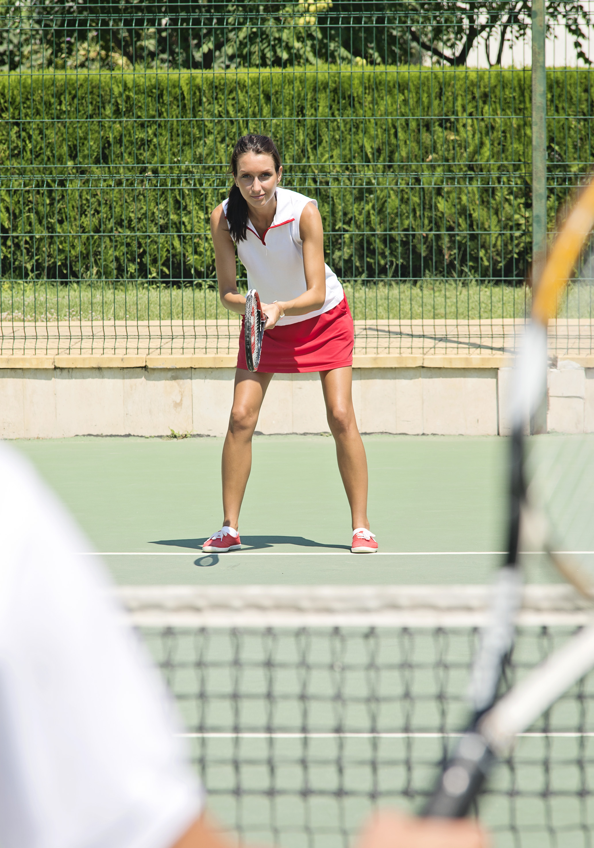 Woman tennis player in red skirt, ready with racket on green court.
