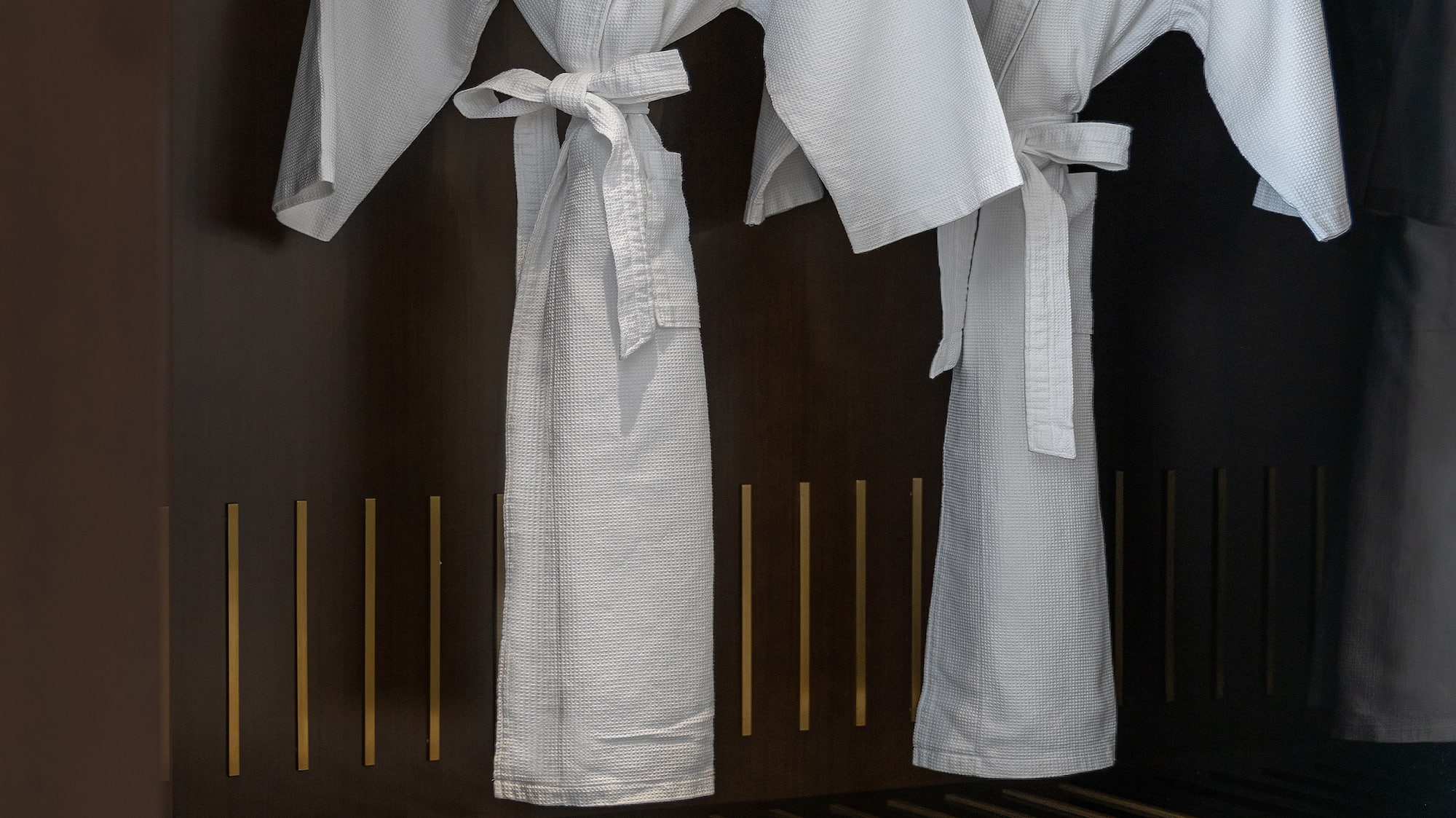 Two white Meliá hotel bathrobes and slippers in a luxury wardrobe.