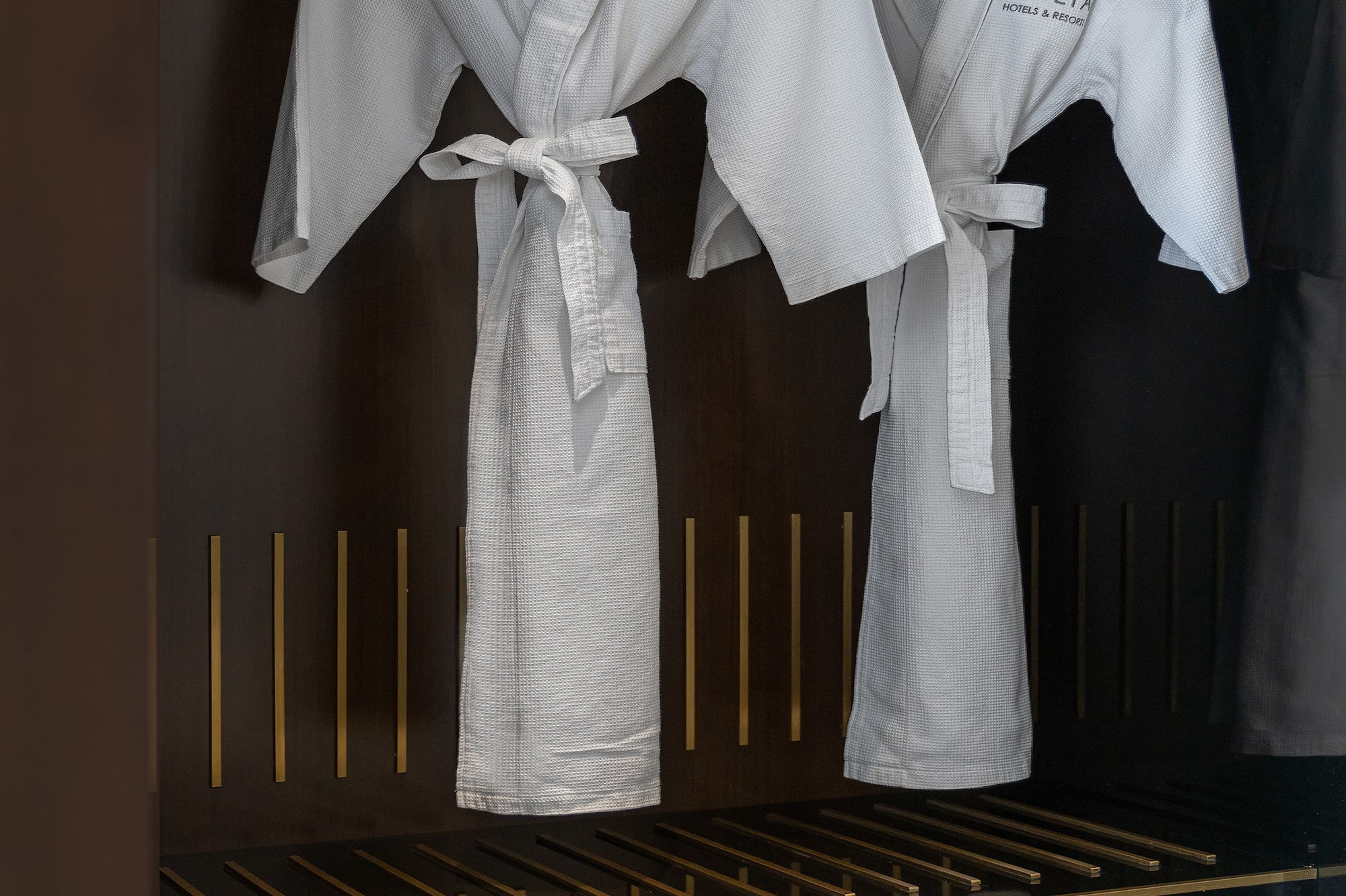 Two white Meliá hotel bathrobes and slippers in a dark wardrobe.