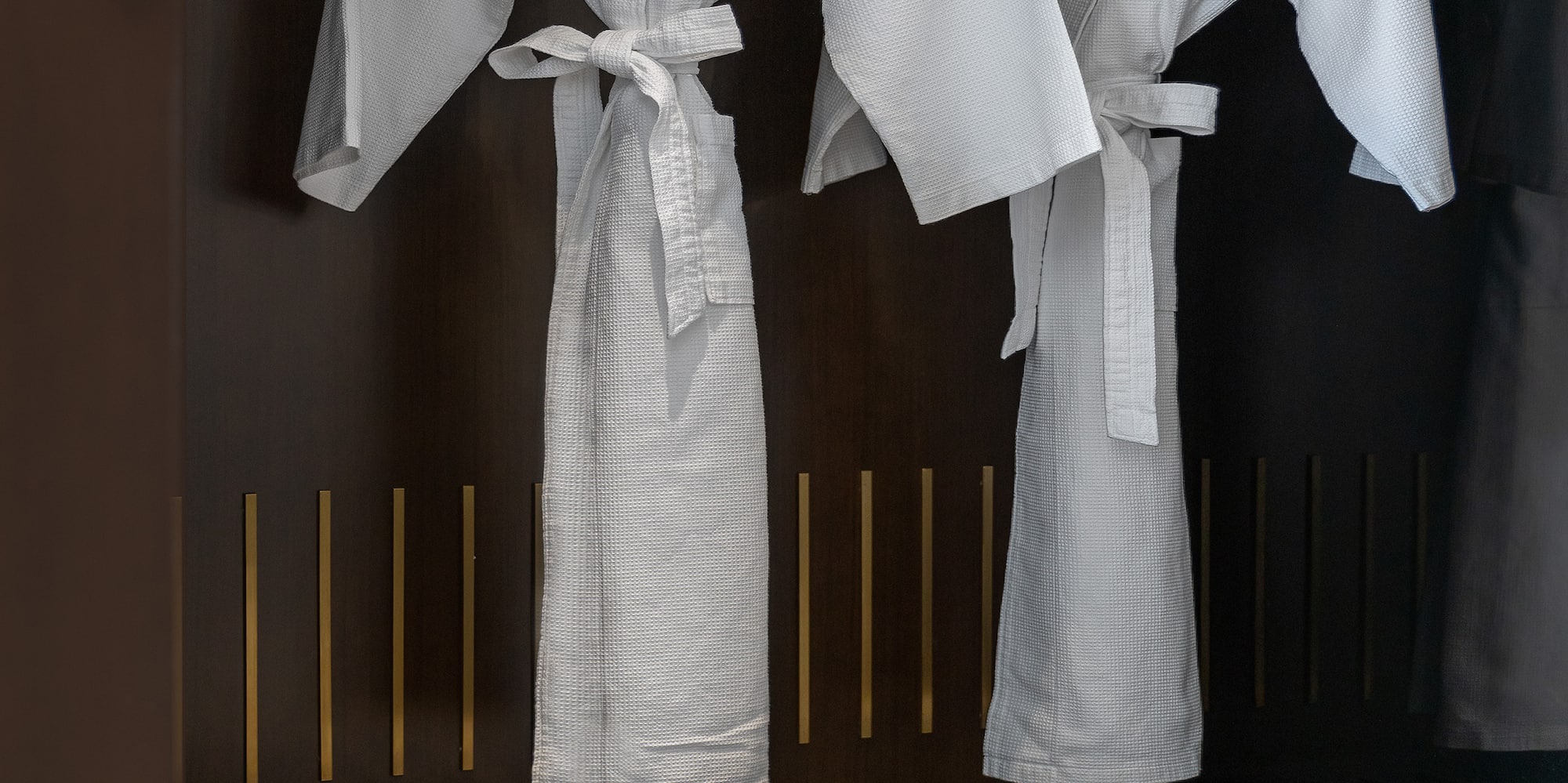 Two white Meliá hotel bathrobes and slippers in a dark wardrobe.