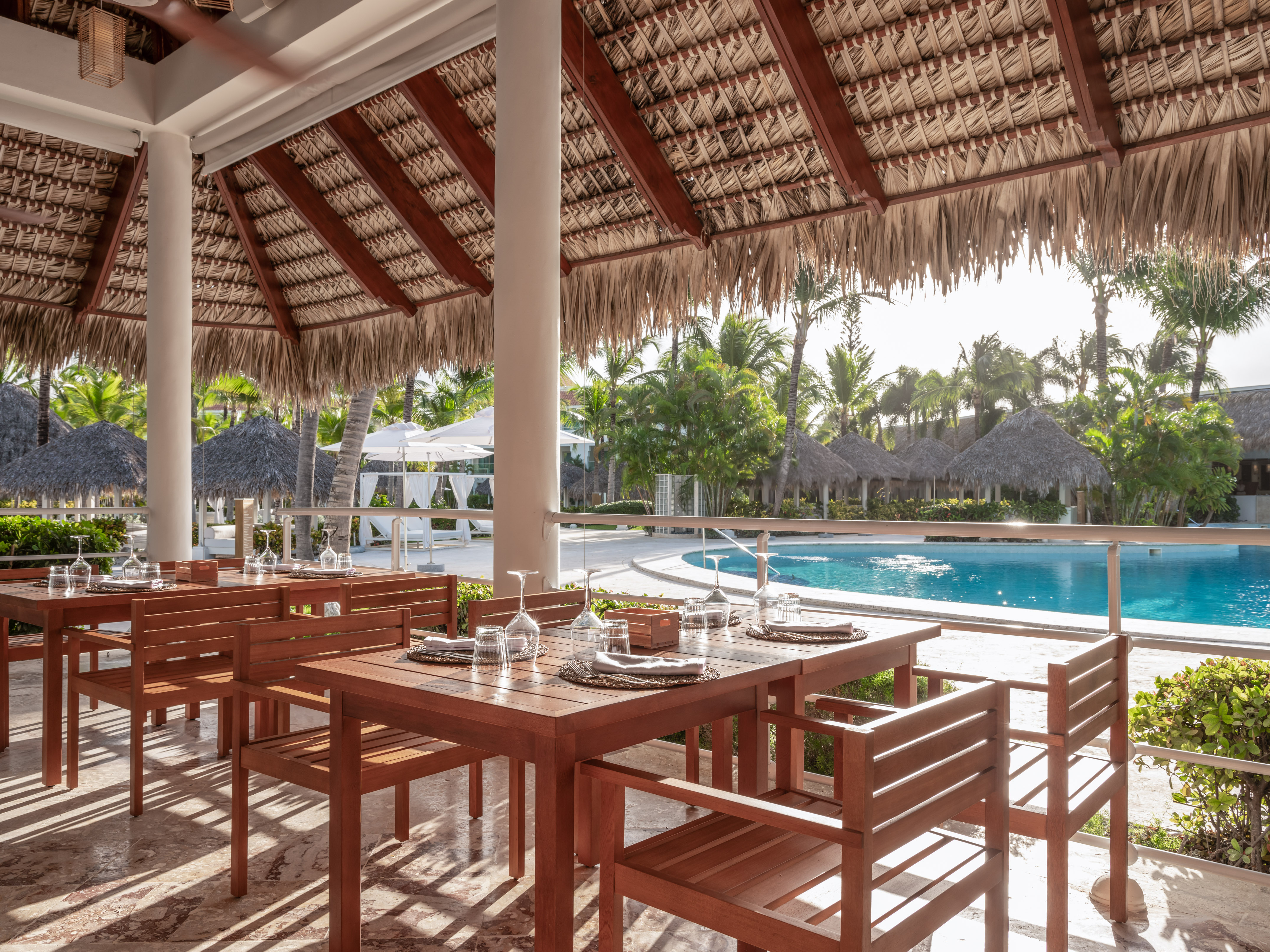 Tropical poolside dining at a resort restaurant under a thatched roof.