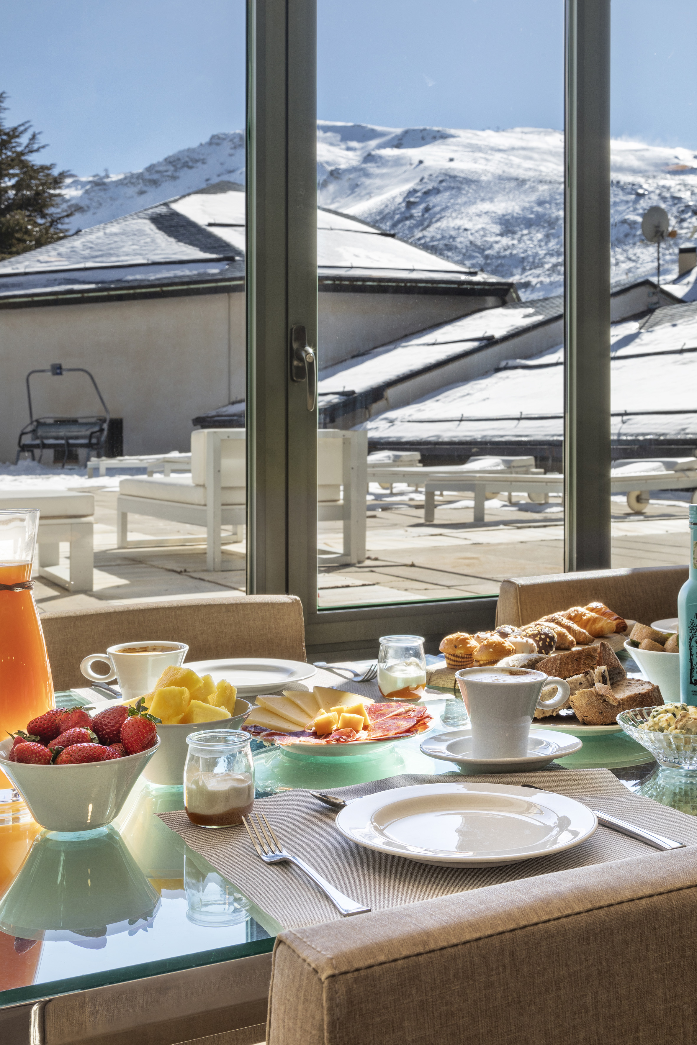 Winter breakfast with fresh fruit, pastries, coffee, overlooking snowy mountains.
