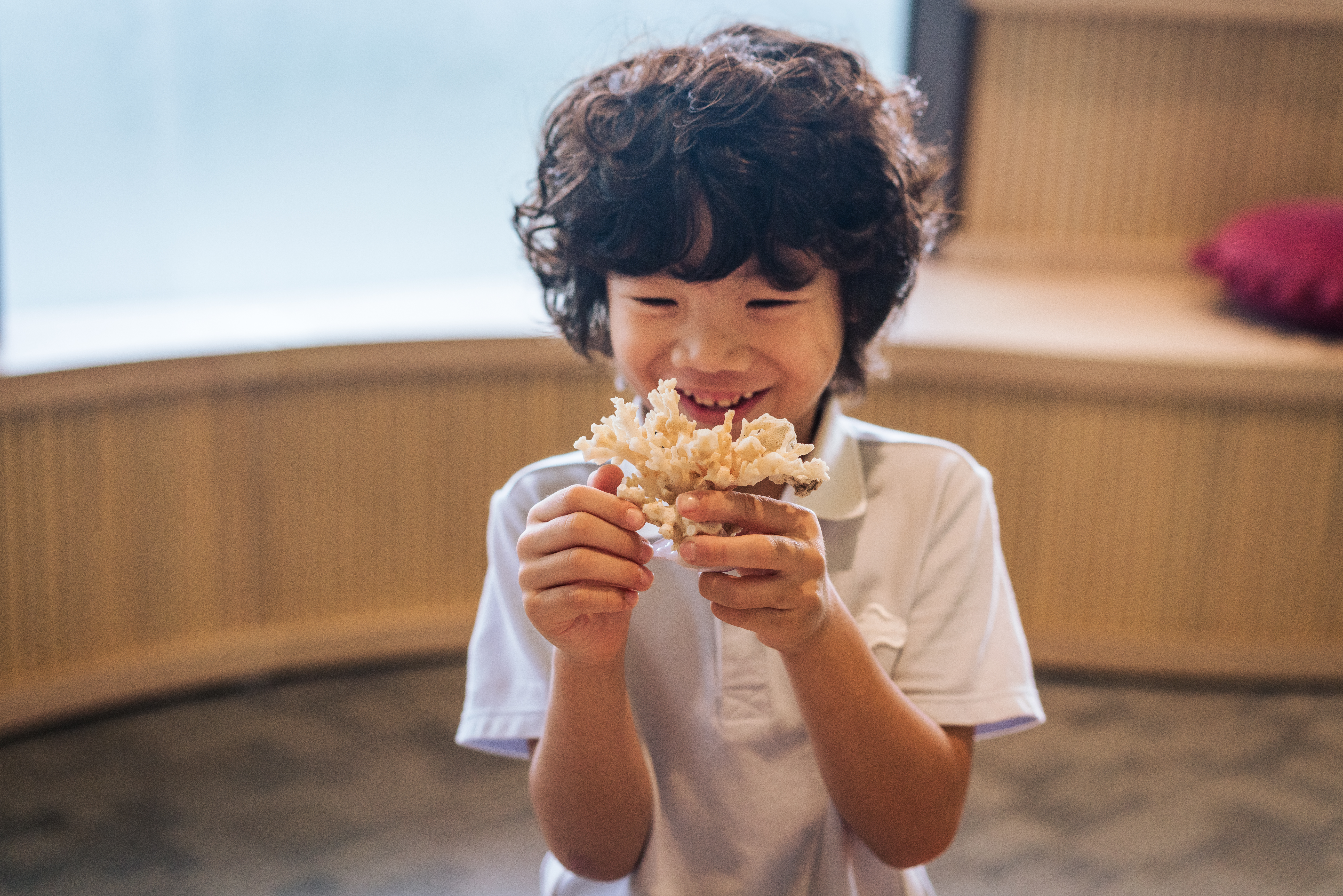 Smiling boy with curly hair examining white coral.