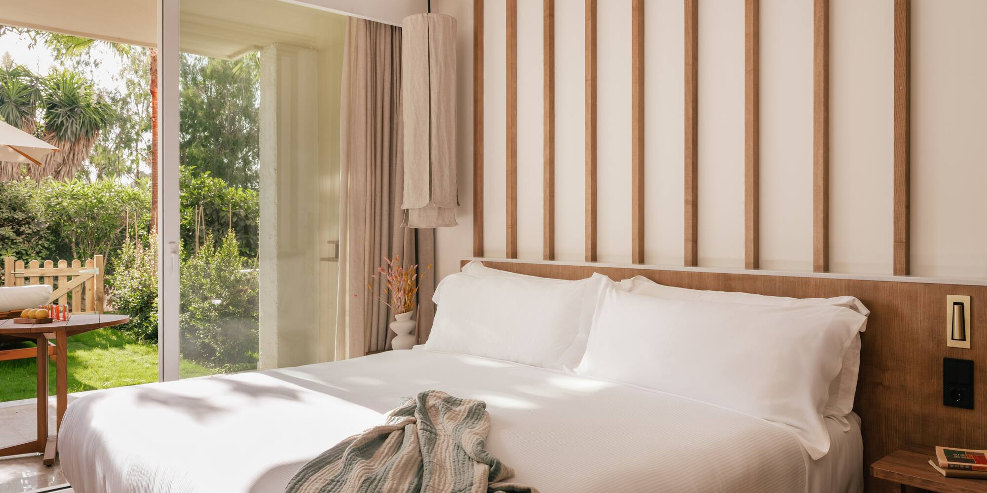 a bed with white sheets and pillows in a room with glass doors